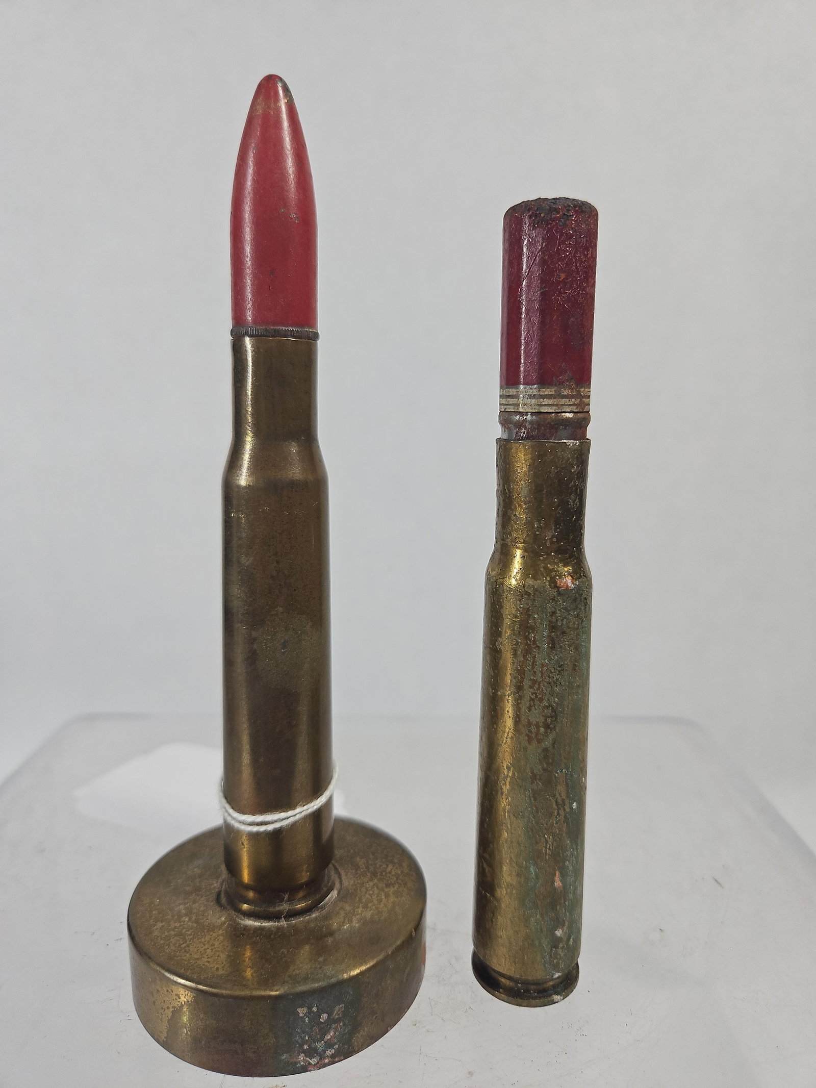 .50 Cal Trench Art & M2 Dummy Round: This lot consists of two vintage inert ordnance-themed items. The first is a trench art style desk accessory featuring a polished brass casing fitted with a pointed, red-painted projectile, securely m