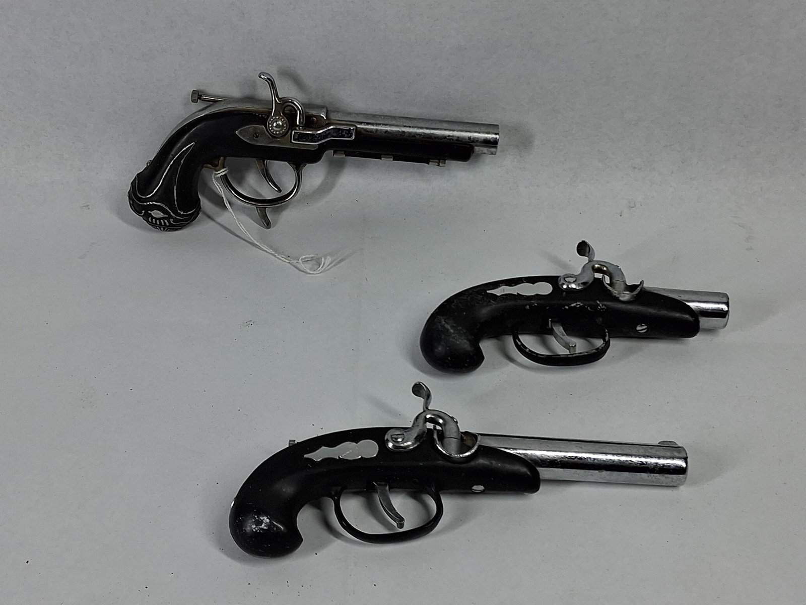 Trio Japanese Replica Pistol Lighters: A Japanese assortment of three miniature cigarette lighters modeled after mid-19th-century firearms. The collection includes one larger flintlock-style pistol and two smaller pocket-sized
