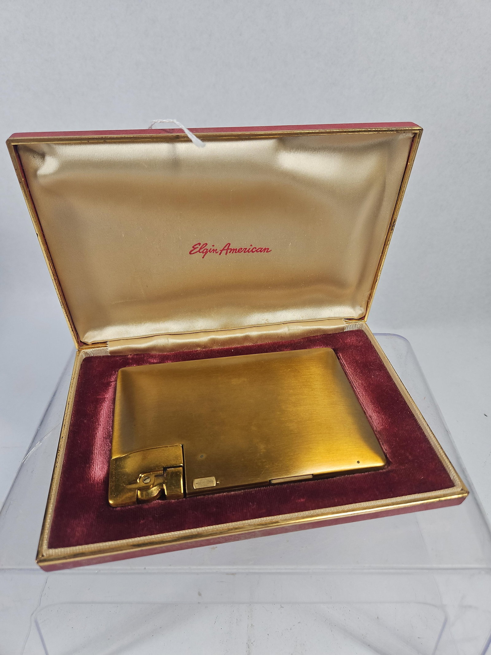 Elgin American Cigarette Case & Lighter: This American-made cigarette case features an integrated flip-top lighter and is presented in its original branded box. The exterior of the rectangular metal case has a gold-toned finish with a