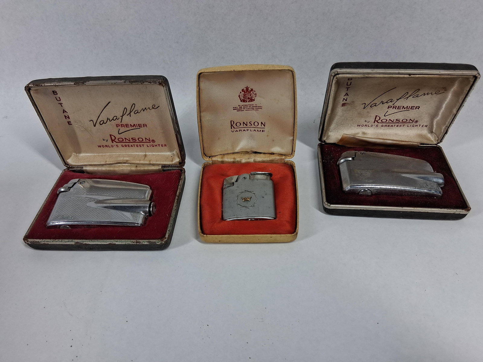 3 Vtg Ronson Varaflame Lighters & Boxes: An assortment of three vintage Ronson Varaflame butane cigarette lighters, each accompanied by a branded presentation case. The collection includes two Varaflame Premier models and one smaller