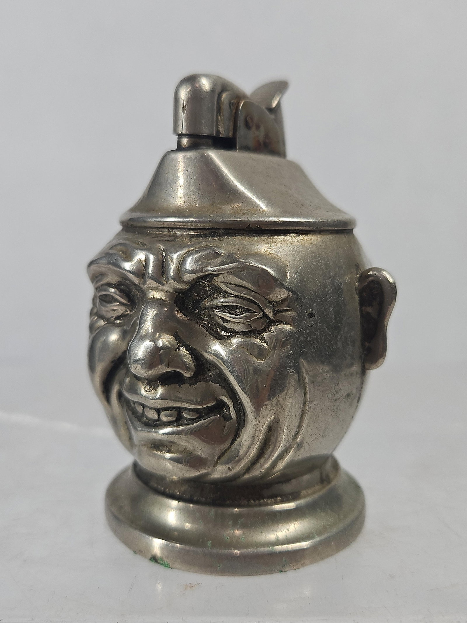 Japanese Metal Caricature Table Lighter: A Japanese novelty table lighter cast in the form of a grinning caricature head. The object is composed of silver-toned cast metal with a figural design featuring exaggerated facial features