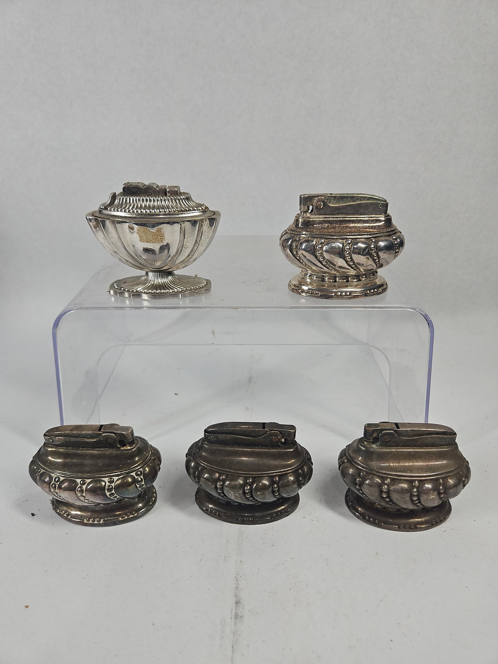 Set Vtg Ronson & A.S.R. Table Lighters: An assortment of American-made silver-plated table lighters featuring decorative lobed and gadrooned metal bodies. The collection includes examples of the Ronson Crown model and a lighter by A.S.R.