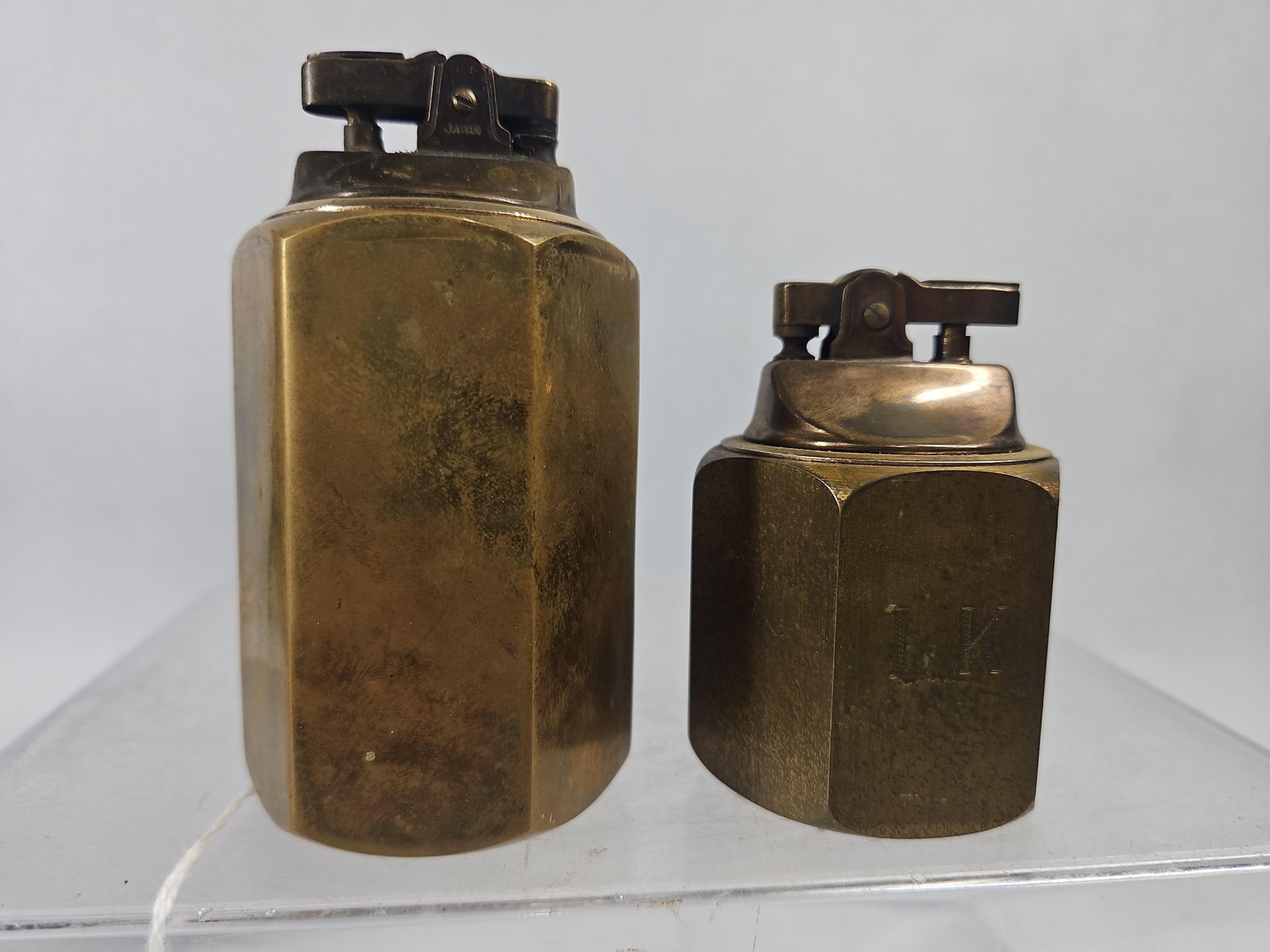 Pair Japanese Hexagonal Brass Lighters: A pair of Japanese solid brass table lighters in two sizes. Each lighter is constructed with a heavy faceted hexagonal brass block base and an integrated metal lift-arm lighting mechanism. The