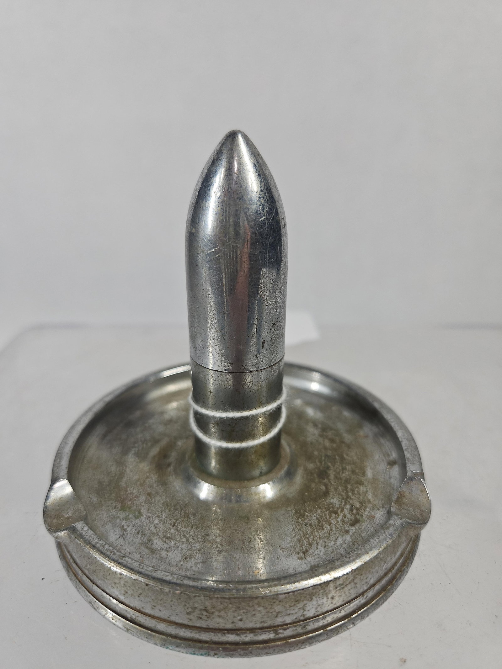 Chrome Montreal Bullet Ashtray/Lighter: A vintage souvenir ashtray and lighter combination constructed from chrome or nickel-plated metal. The piece features a circular base with two integrated cigarette rests. Rising from the center is a v