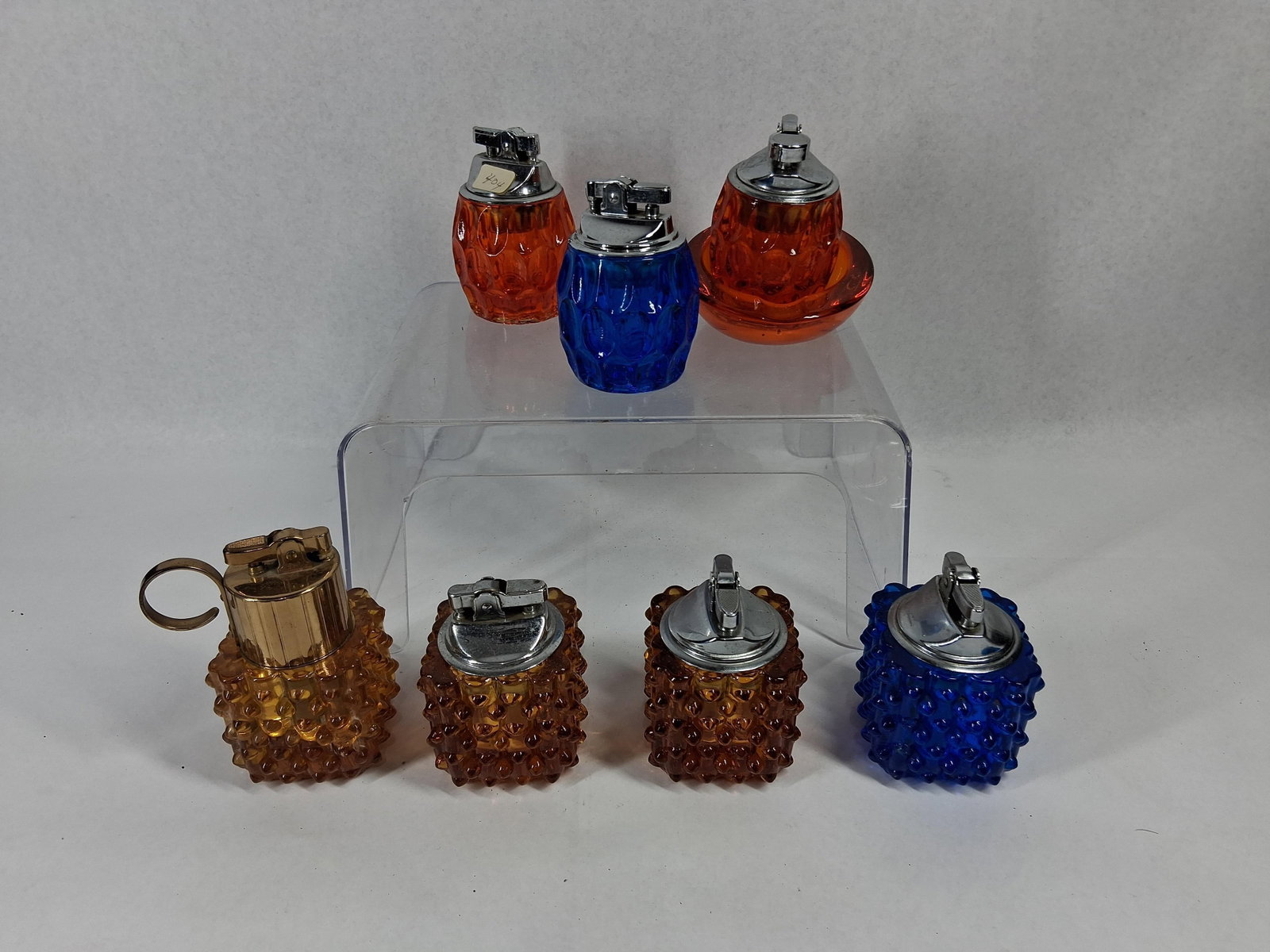 8 Vtg Pressed Glass Lighters & Ashtray: An assortment of eight vintage glass items including seven table lighters and one matching ashtray base, featuring two distinct pressed glass patterns. The collection includes pieces with a hobnail