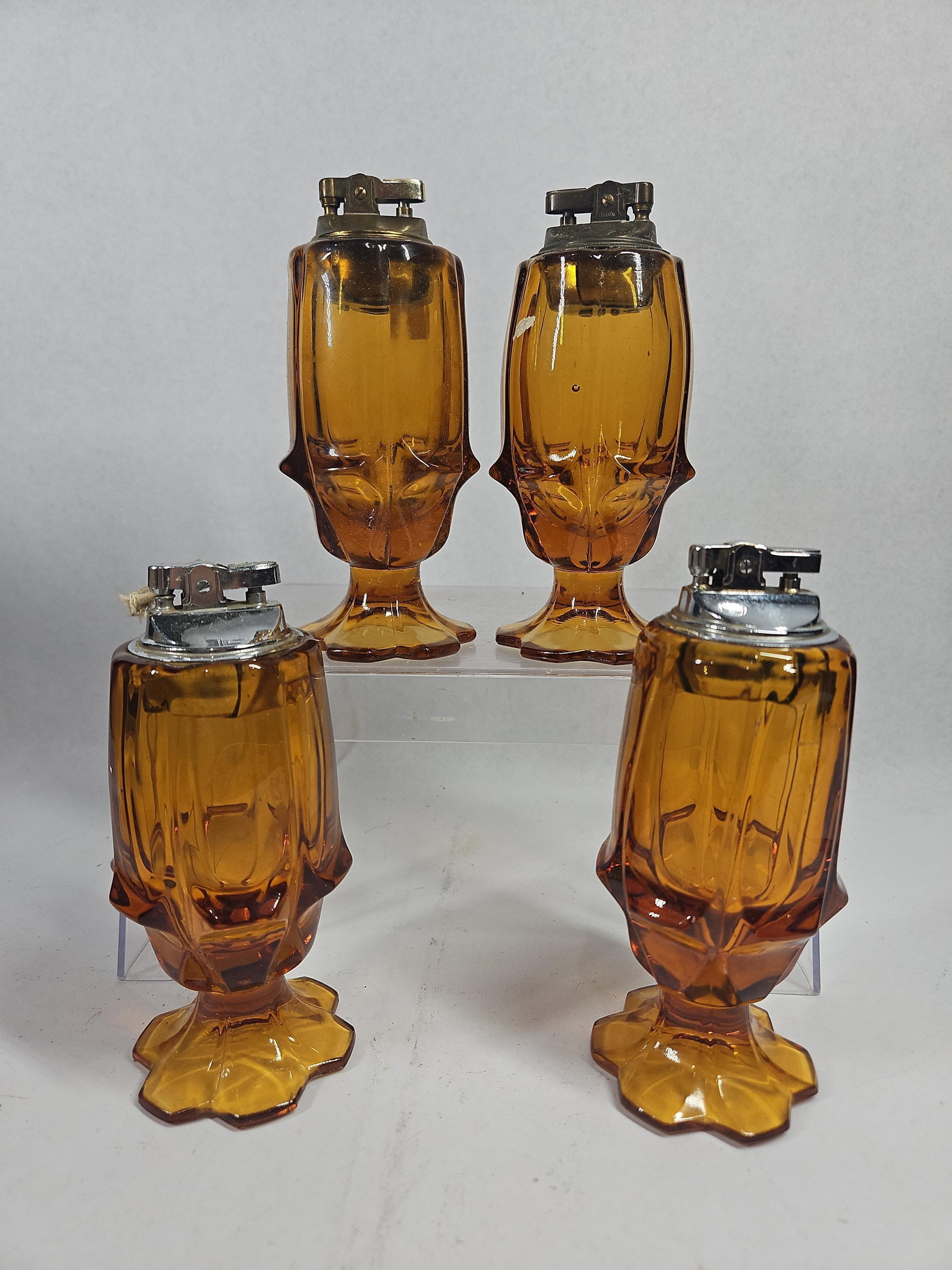 Set Japanese Amber Glass Table Lighters: A set of Japanese faceted amber glass table lighters featuring footed, geometric bodies. The glass is a deep amber color, decorated with a pattern of faceted thumbprint-style indentations and