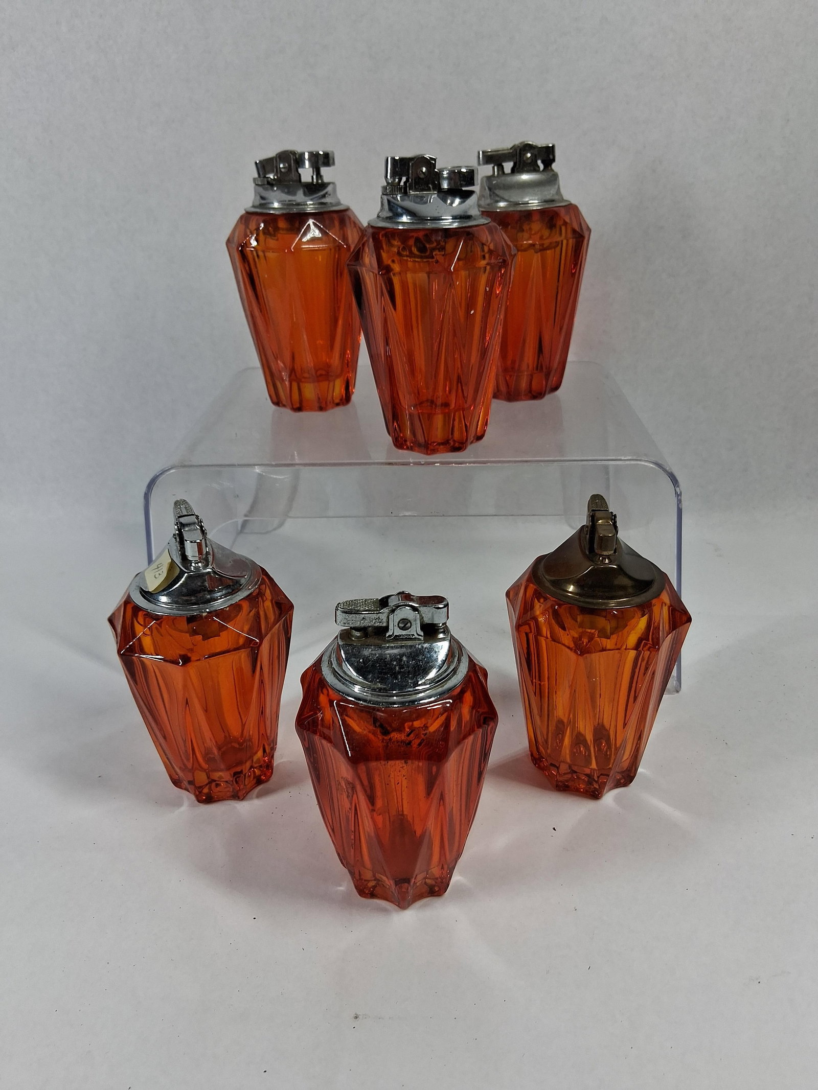 Vtg Amber Faceted Glass Table Lighters: An assortment of mid-century modern table lighters featuring translucent amber glass bases. The molded glass bases are designed in a tapered, multi-faceted geometric form. Each unit is fitted with a