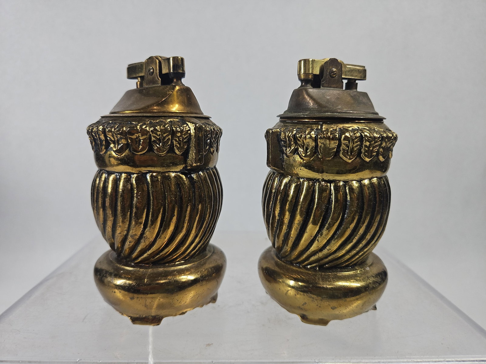 Pair Evans USA Gilt Cast Table Lighters: A pair of American gilt cast metal table lighters designed in a Neoclassical urn form. Each vessel is decorated with a band of acanthus leaf molding positioned above a gadrooned, spirally fluted