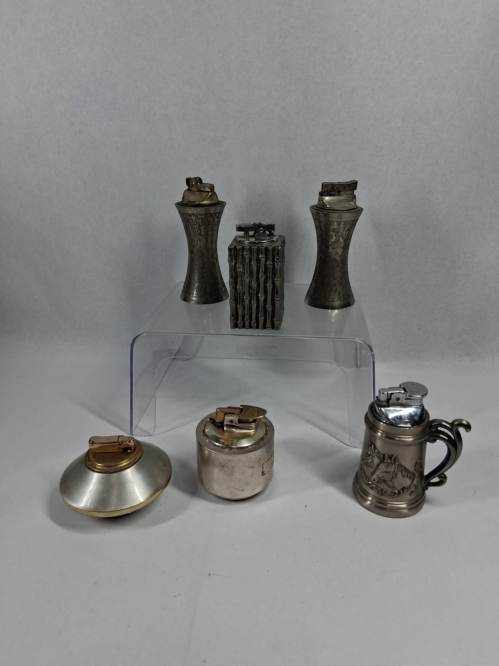 Colibri & Delli Metal Table Lighters: An Indian engraved metal lighter with an hourglass form featuring floral scrollwork, with characters impressed on the base reading W. G. C. INDIA (photo 7). A similar hourglass-form lighter bears an