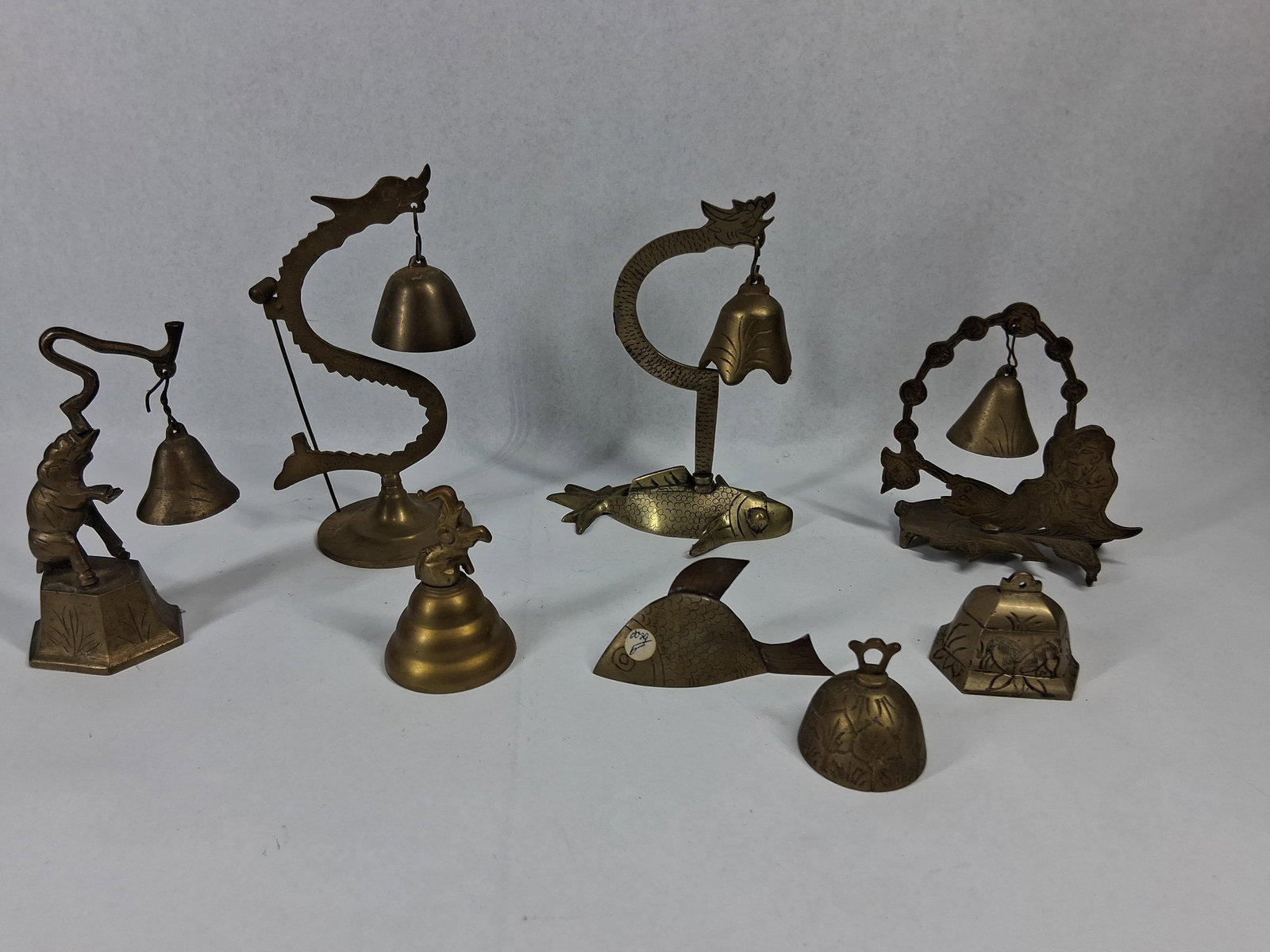 Set 10 Chinese Brass Bells & Stands: A Chinese cast brass collection comprising ten pieces, featuring various ornamental stands and individual bells decorated with traditional motifs. The group includes an S-curved dragon bell stand
