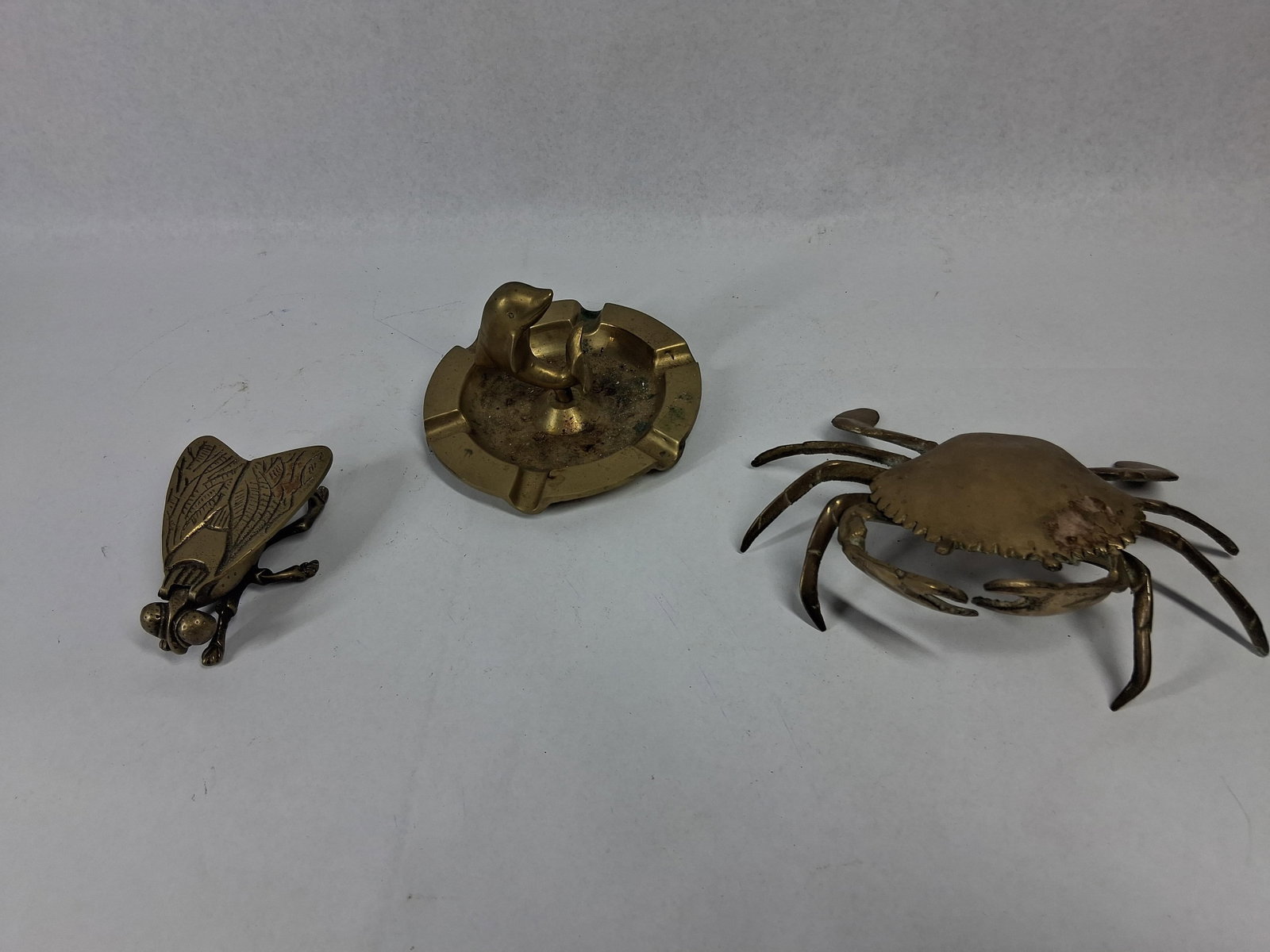 3 Brass Animal Novelty Ashtrays & Boxes: This collection consists of three cast brass decorative objects in animal forms. The group includes a circular ashtray featuring four integrated cigarette rests and a central figure of a leaping