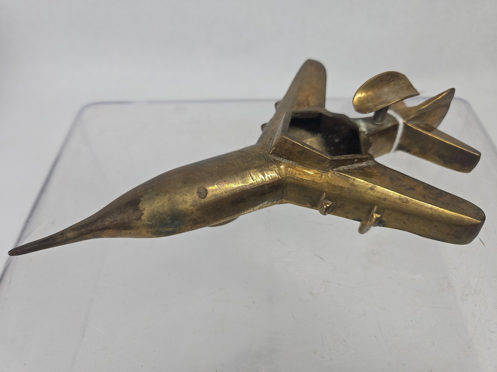 Vtg Cast Brass Jet Fighter Ashtray: A solid cast brass model of a stylized jet fighter aircraft, designed for use as a desk accessory. The fuselage features a recessed central cavity intended for use as an ashtray. A swiveling,
