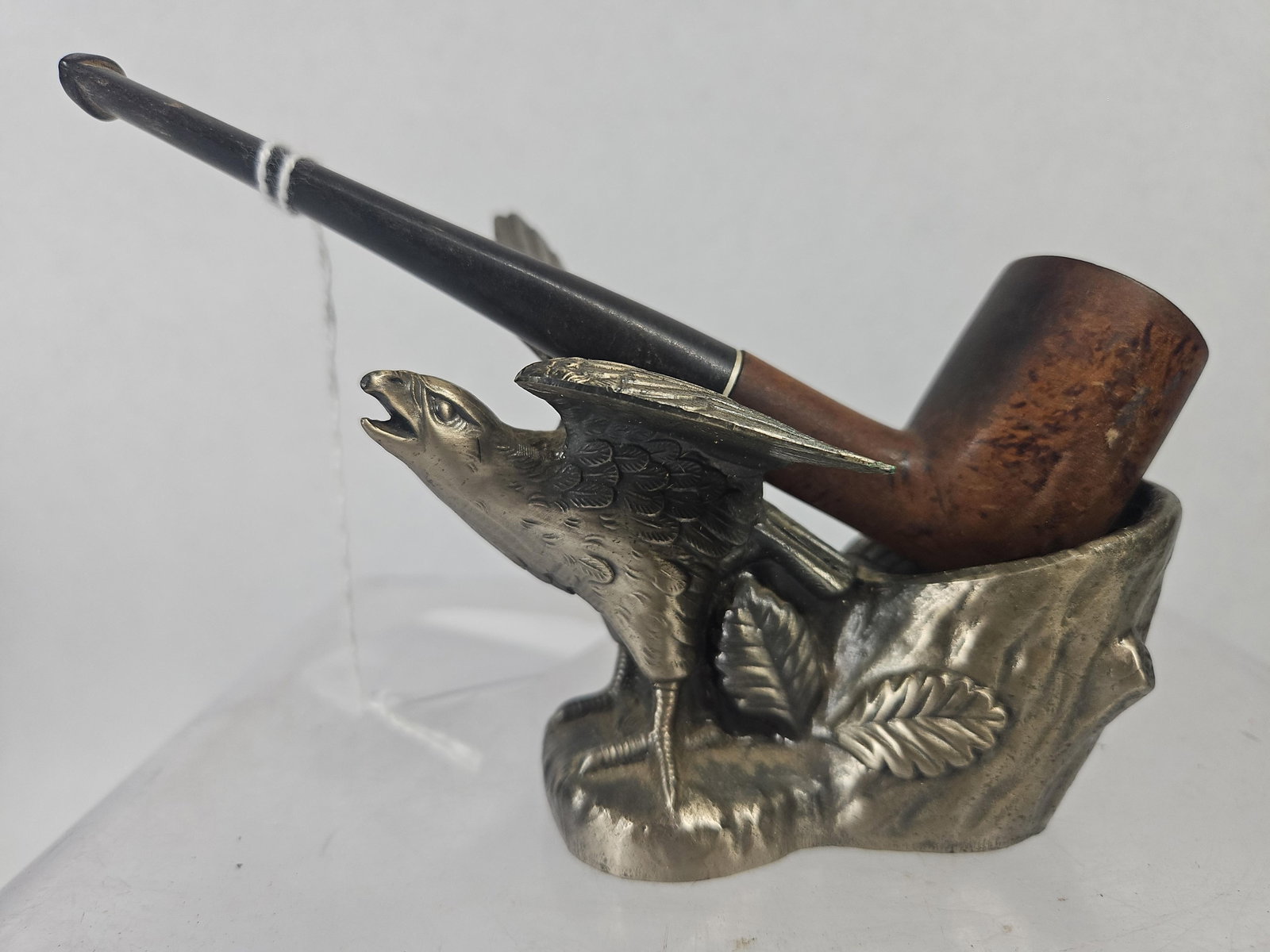 Briar Wood Pipe & Figural Eagle Stand: A two-piece smoking set consisting of a wood pipe and a cast metal stand. The pipe features a briar wood bowl with a black tapered stem and a white band at the shank junction. The stand is made of