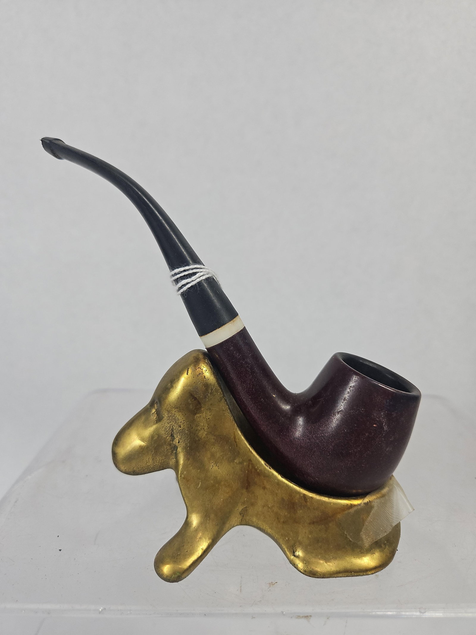 Medico Apollo Pipe & Brass Dog Stand: A vintage smoking pipe and a novelty metal pipe stand. The pipe is constructed with a dark reddish-brown finished bowl and shank, joined to a curved black stem. A white decorative ring is set at the