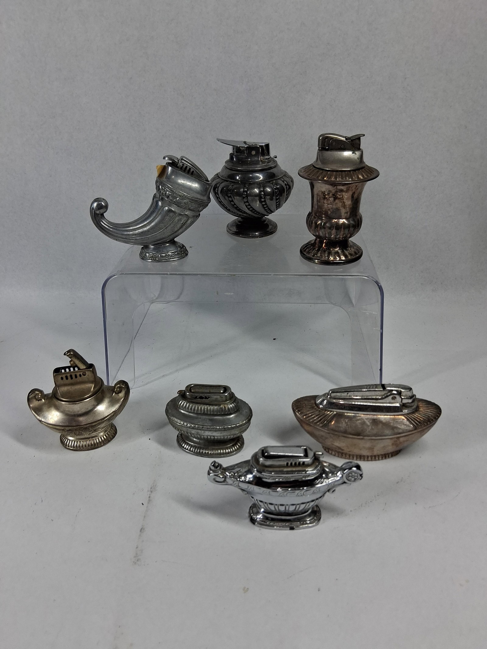 Ronson & Canterbury Vtg Table Lighters: A collection of metal table lighters in various decorative forms including urns, boat shapes, a cornucopia, and Aladdin-style oil lamps. The assortment features pieces finished in silver plate and chr