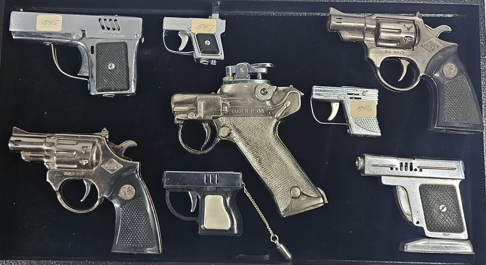 Vtg Cast Firearm Lighters: Luger/Laurel: An assortment of vintage novelty cigarette lighters designed in the form of various handguns, primarily constructed from cast metal with silver-tone and chrome-tone finishes. A large central lighter