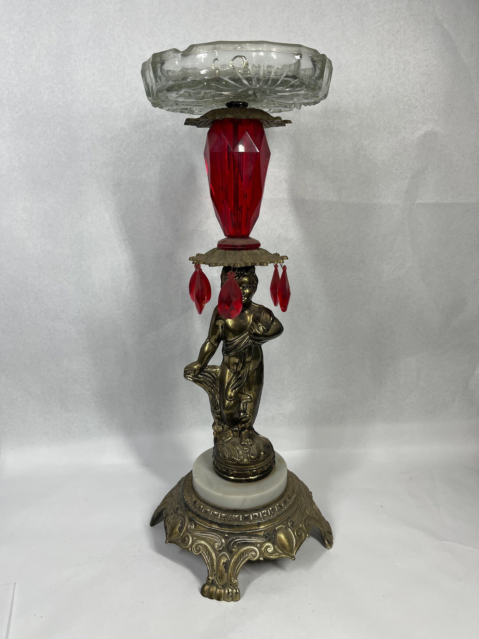 Vtg Cherub Ashtray Stand w/ Ruby Prisms: A vintage tabletop ashtray stand featuring a central cast metal figure of a standing, partially draped cherub or putto. The figure is finished in a gold tone and stands upon an ornate, four-footed cas