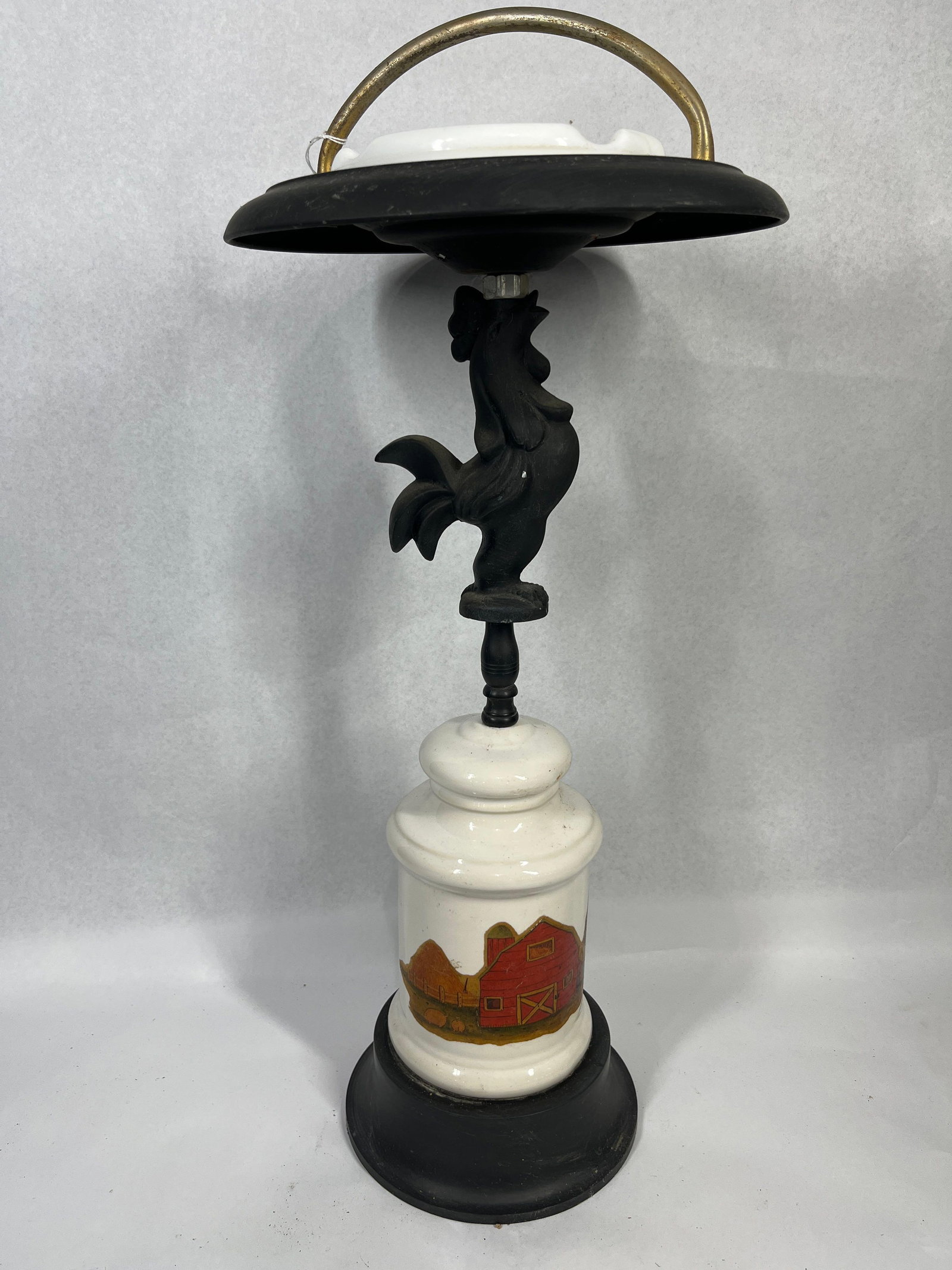 Rooster Smoking Stand w/ Milk Glass: This vintage pedestal smoking stand features a mid-century Americana design. The assembly consists of a circular black-finished metal base supporting a central white ceramic jar-shaped vessel. The