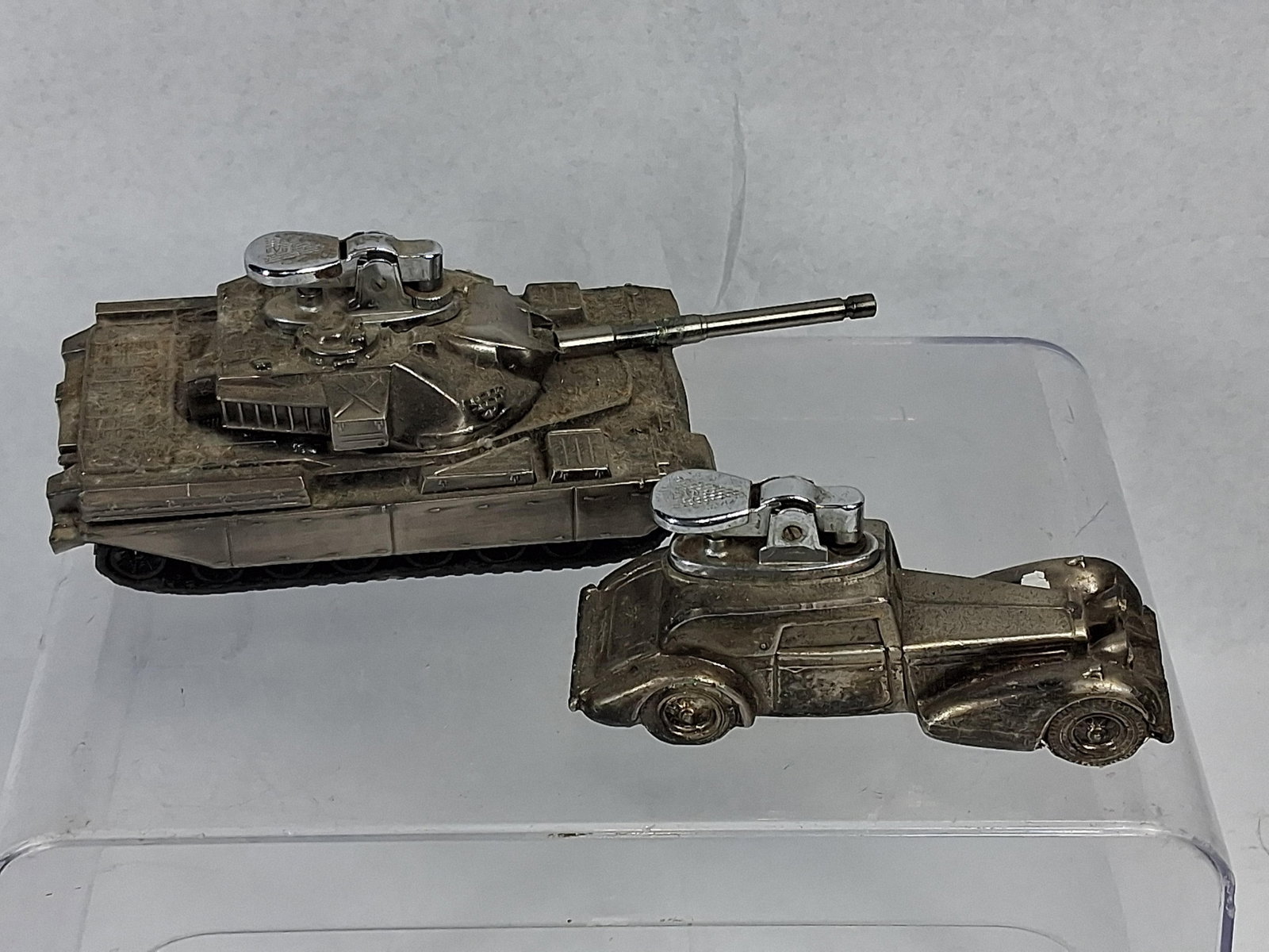 Pair Japanese Metal Tank & Car Lighters: Two silver-tone plated die-cast metal novelty table lighters manufactured in Japan. The first is a detailed model of a British Chieftain Main Battle Tank. The gas-powered lighter mechanism is