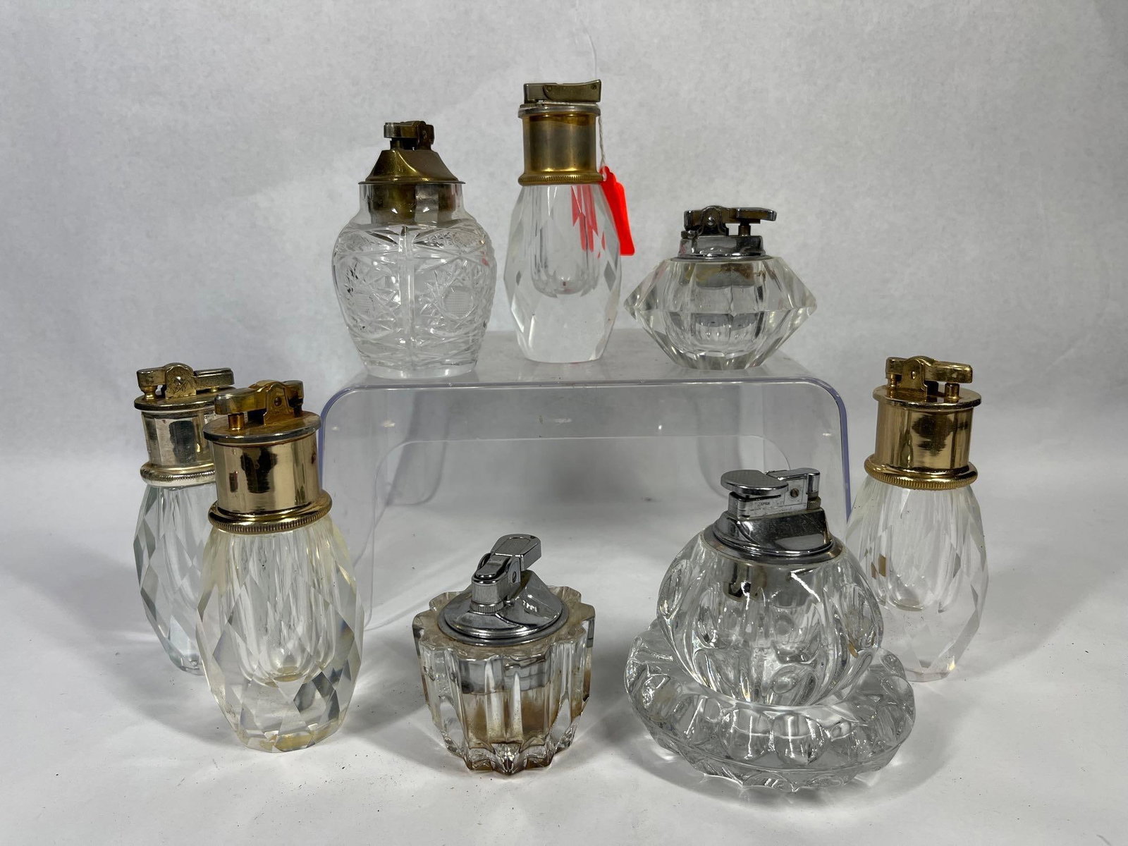 Vtg Glass & Crystal Lighters & Ashtray: A collection of table lighters featuring various clear glass and cut crystal bases, together with a small molded glass ashtray. The assortment includes bases in ovoid, faceted, and ribbed forms,
