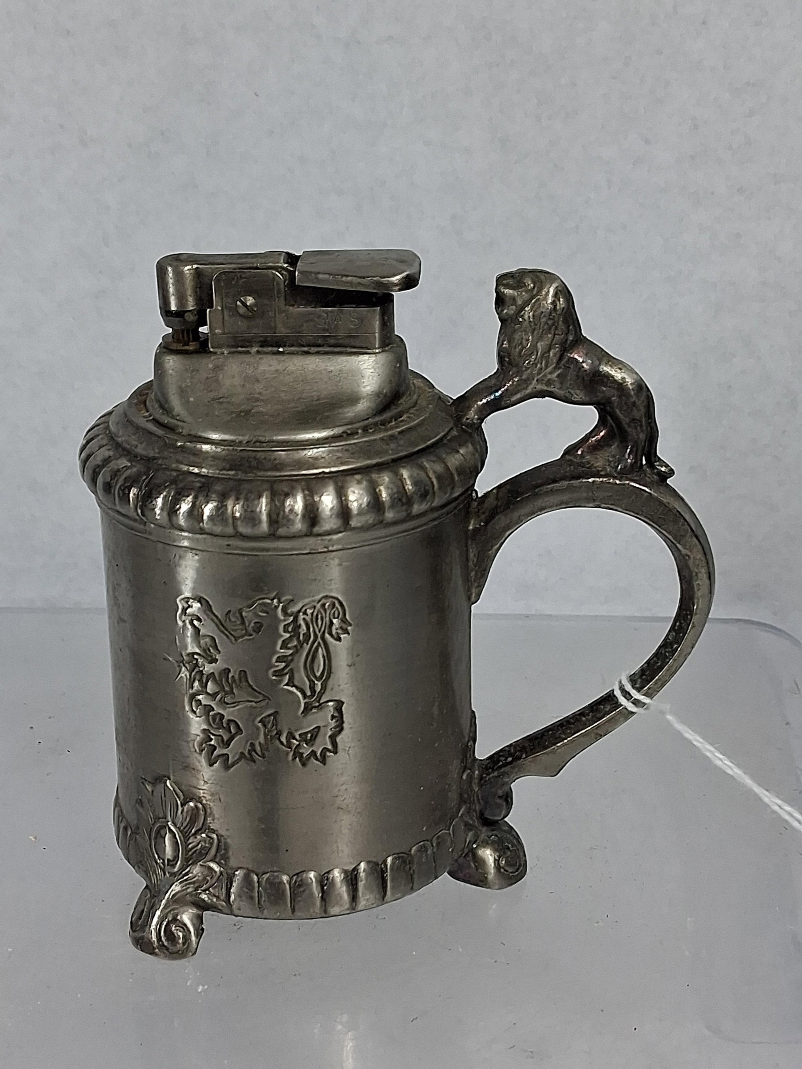 Silver-Plate Lion Tankard Table Lighter: This vintage novelty table lighter is constructed of silver-plated base metal in the form of a miniature footed tankard. The cylindrical body features a relief-cast heraldic lion rampant. The curved h