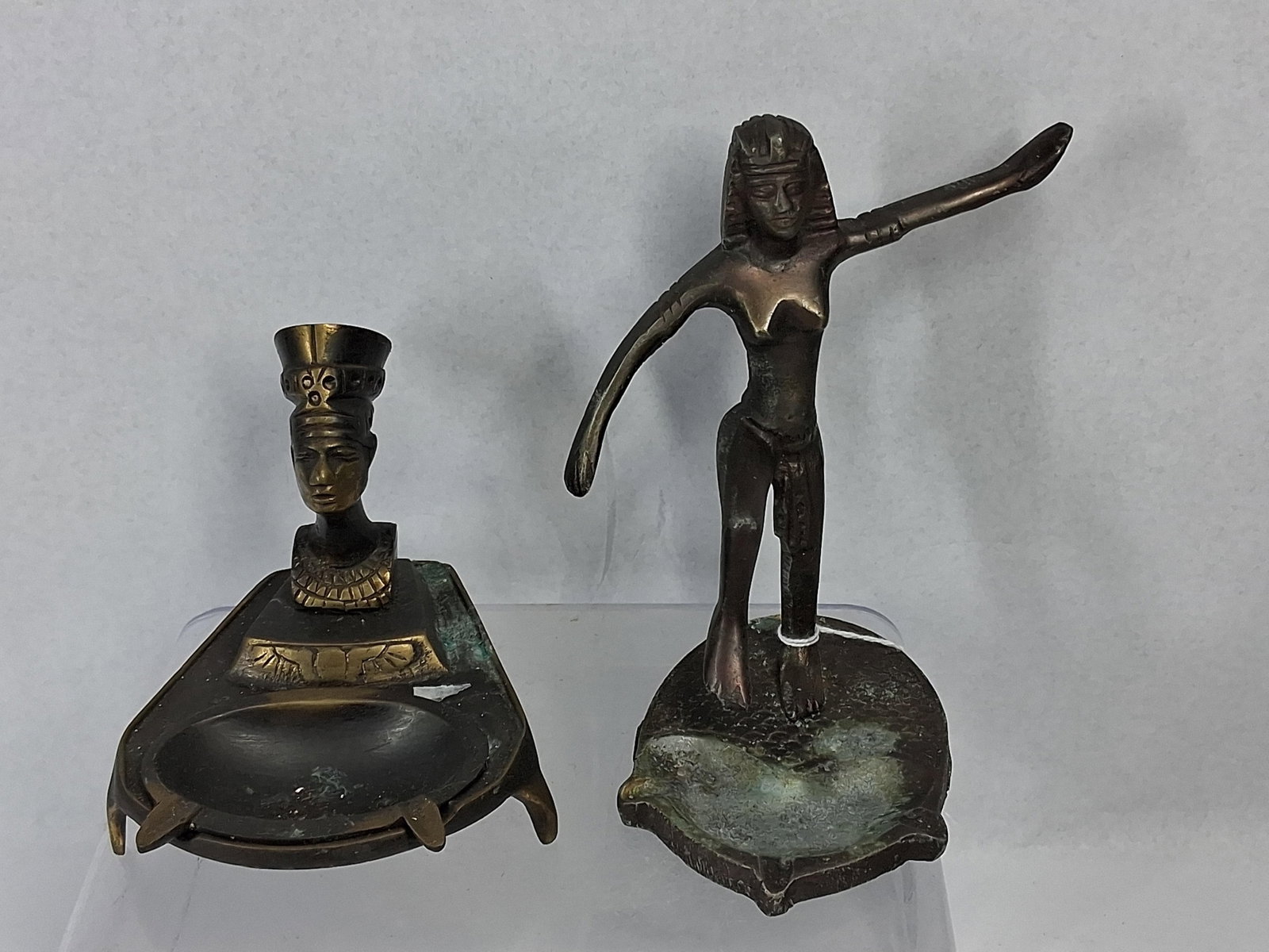 Egyptian Revival Cast Metal Ashtrays: This lot consists of two cast metal desk accessories in the Egyptian Revival style, constructed from cast brass or bronze with a dark patina. The first piece is a pedestal-style ashtray featuring a