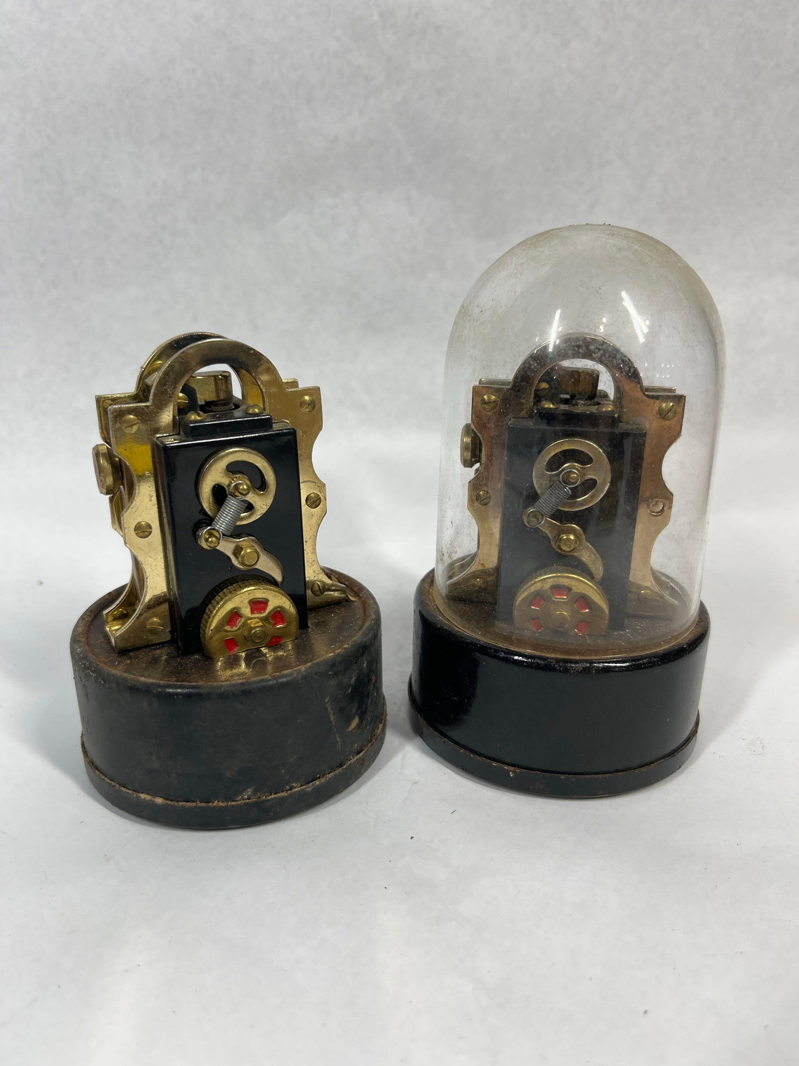 Pair Japanese Stock Ticker Lighters: A pair of Japanese table lighters designed as miniature replicas of nineteenth-century stock ticker machines. Each unit features a central black plastic housing secured within a brass-plated metal sup