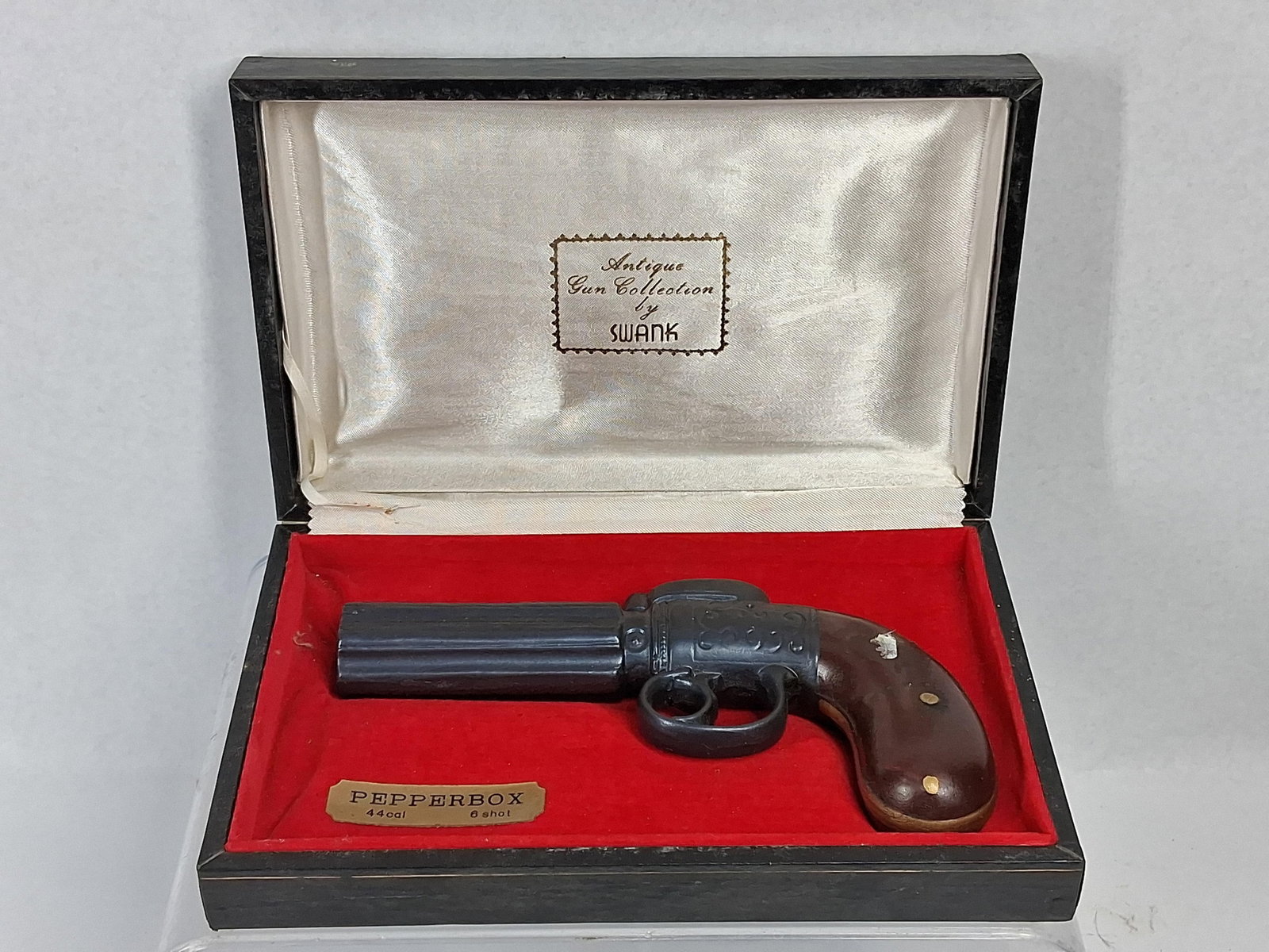 Swank Pepperbox Gun Lighter w/ Orig Box: A vintage Swank novelty table lighter modeled after a 19th-century pepperbox pistol. The body is constructed of cast metal with a dark gray gunmetal finish and features scrolled decorative engraving o