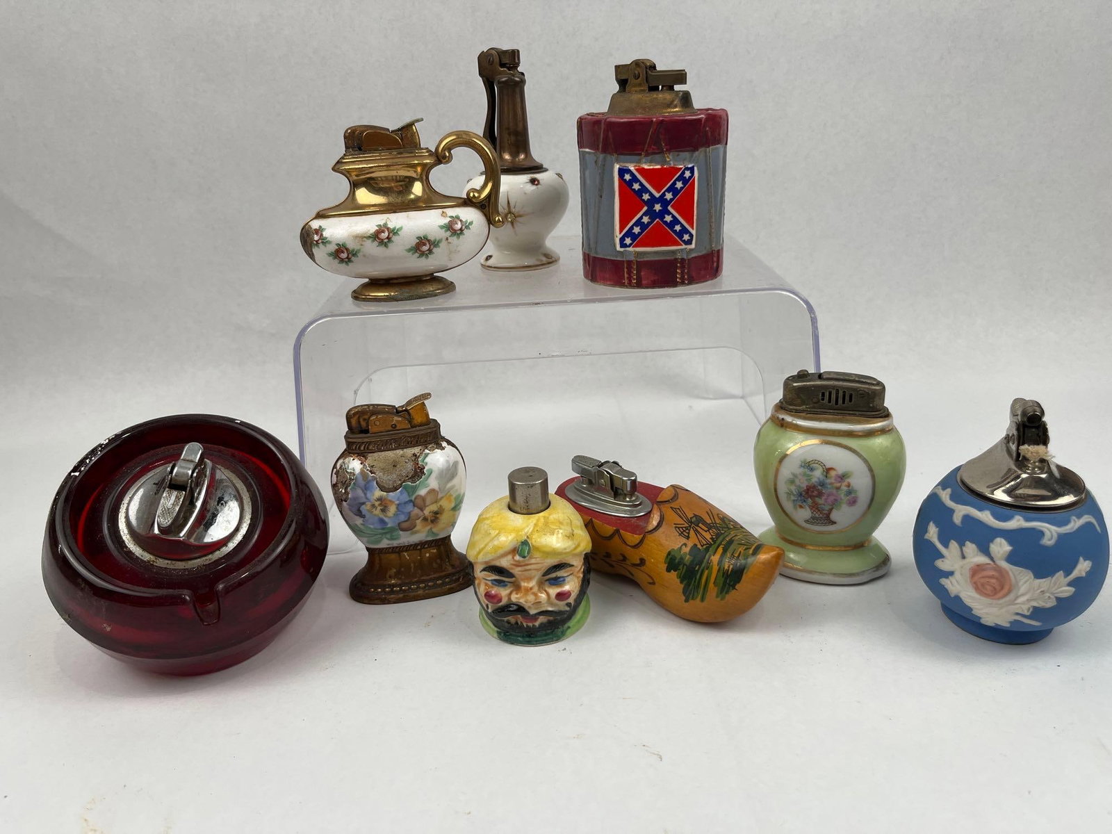 Shafford Japan & Novelty Table Lighters: This collection of table lighters features a variety of forms constructed from ceramic, glass, and wood. A drum-shaped ceramic lighter is decorated with a Confederate battle flag motif; its underside