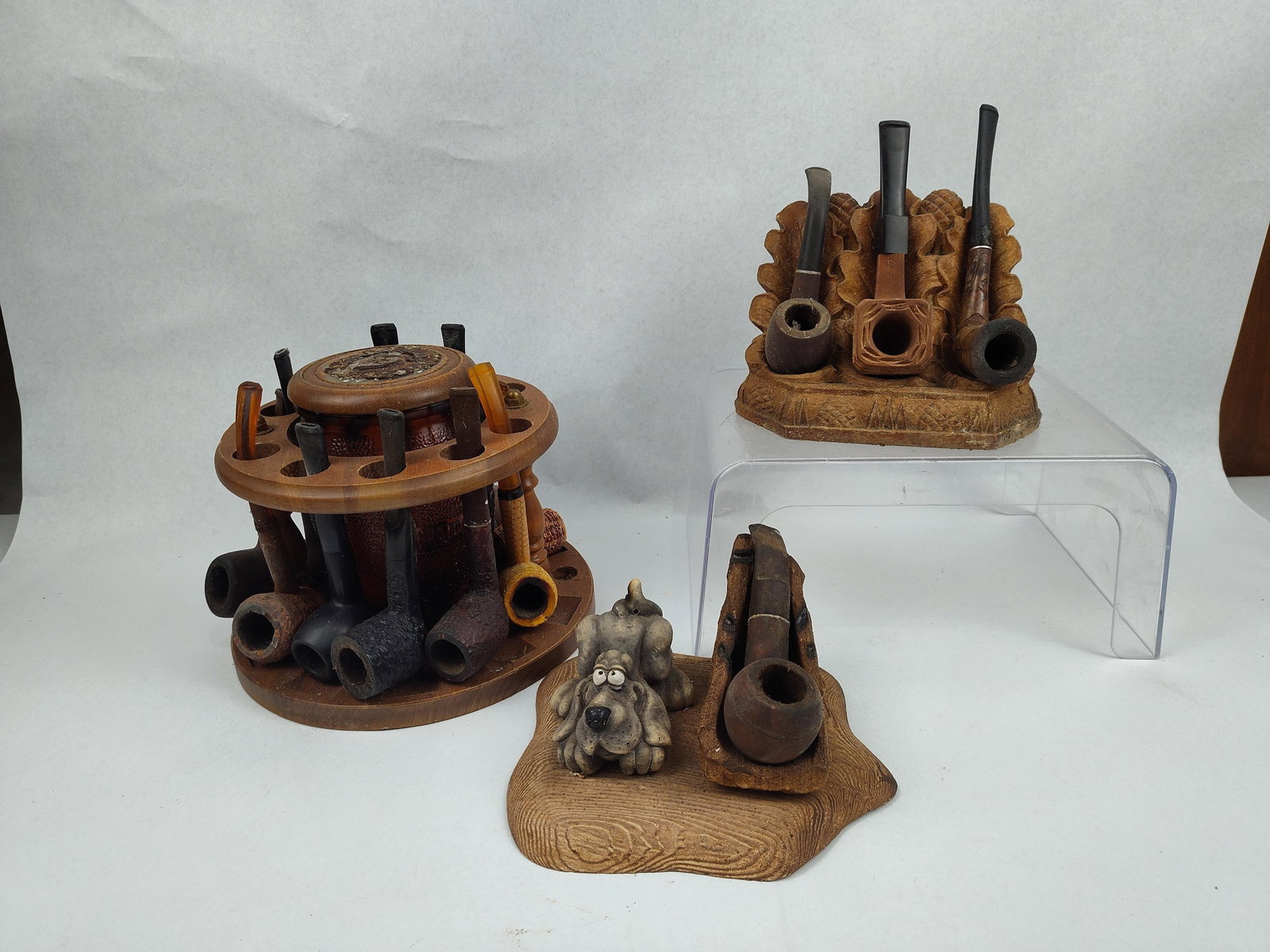 Vtg Smoking Pipes, Stands & Humidor Set: This collection of smoking accessories includes a circular wooden pipe rack, an amber glass humidor, and two decorative cast pipe stands. The central assembly features a circular wooden rack with