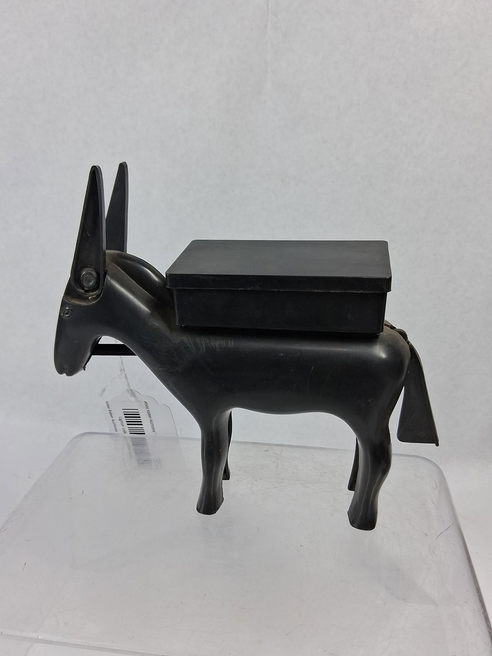 Vtg Plastic Donkey Cigarette Dispenser: A novelty cigarette dispenser designed in the form of a standing donkey, constructed from black molded plastic. The figure features a rectangular reservoir box mounted on its back, fitted with a