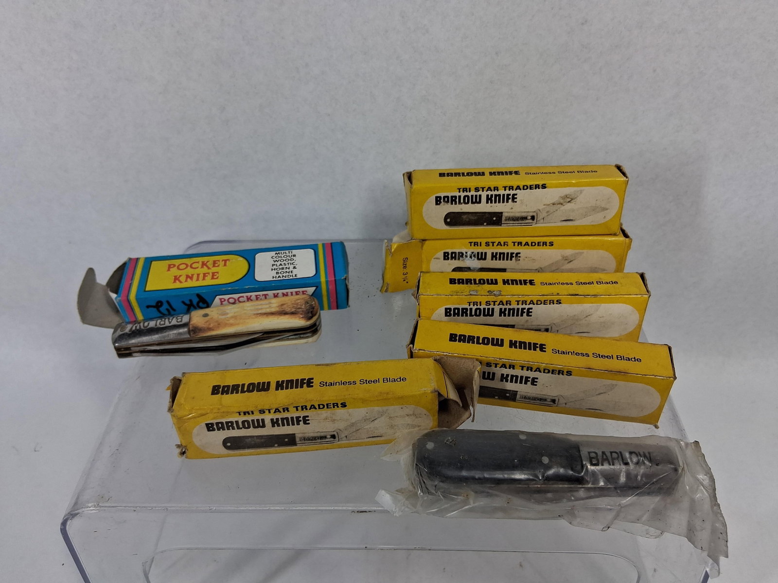 7 Tri Star Traders Barlow Pocket Knives: An assortment of seven Barlow-pattern folding pocket knives, six of which are accompanied by their original retail boxes. The lot includes five yellow boxes printed in black with the text TRI STAR