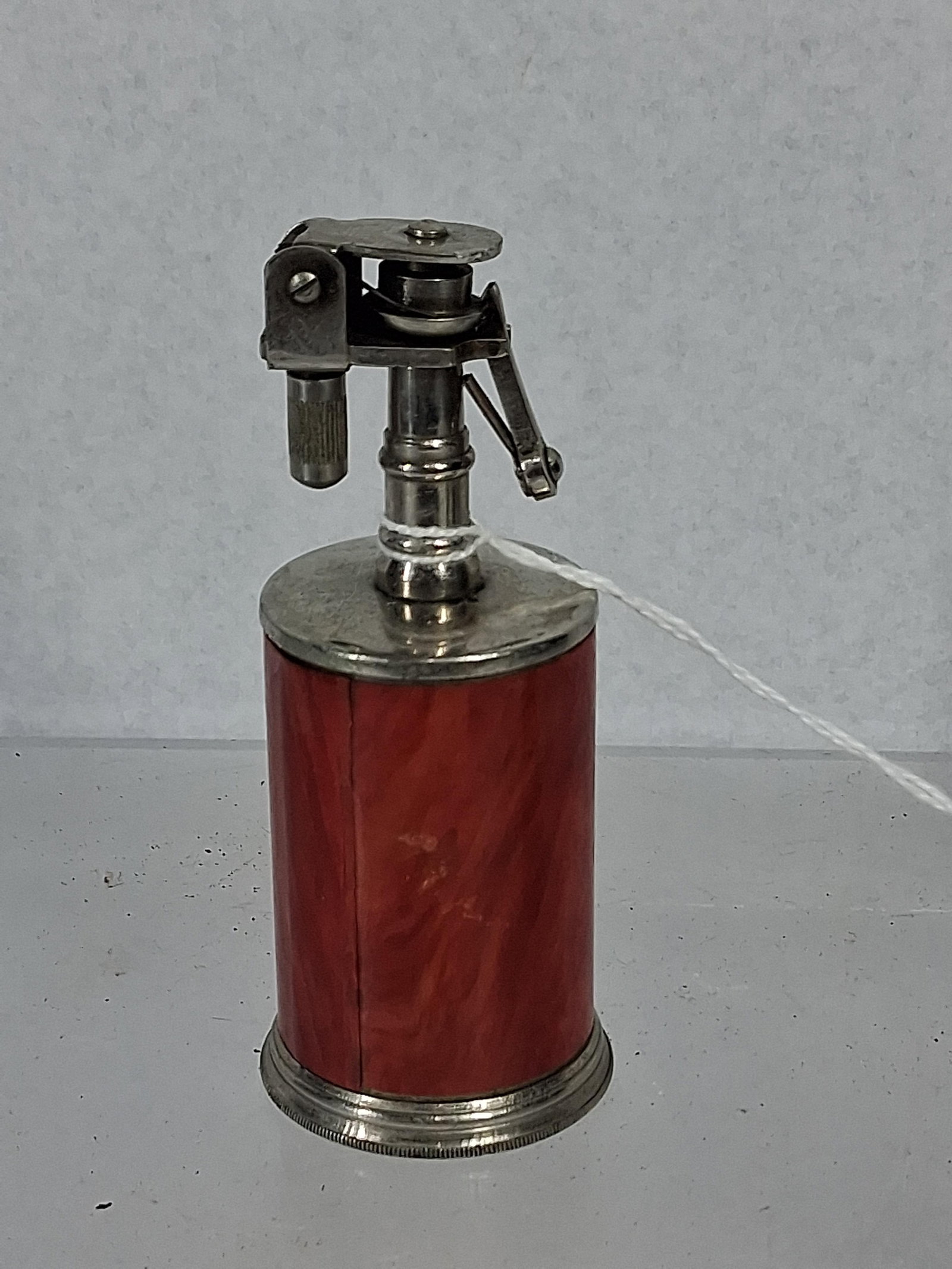 Japanese Marbled Lift-Arm Table Lighter: A Japanese vintage lift-arm table lighter featuring a cylindrical body wrapped in a red marbled celluloid sleeve. The lighter utilizes a chrome-plated metal lift-arm mechanism, including a striker whe
