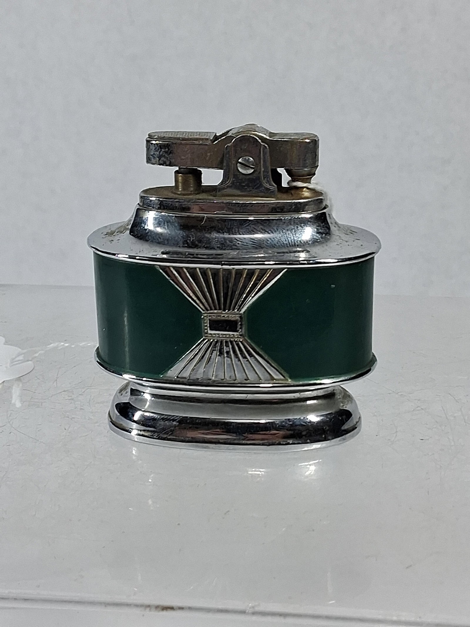 Japanese Excello Art Deco Table Lighter: A Japanese chrome-plated metal table lighter featuring an Art Deco design with inset dark green panels on the front and back. The body is decorated with a central chrome sunburst or hourglass motif