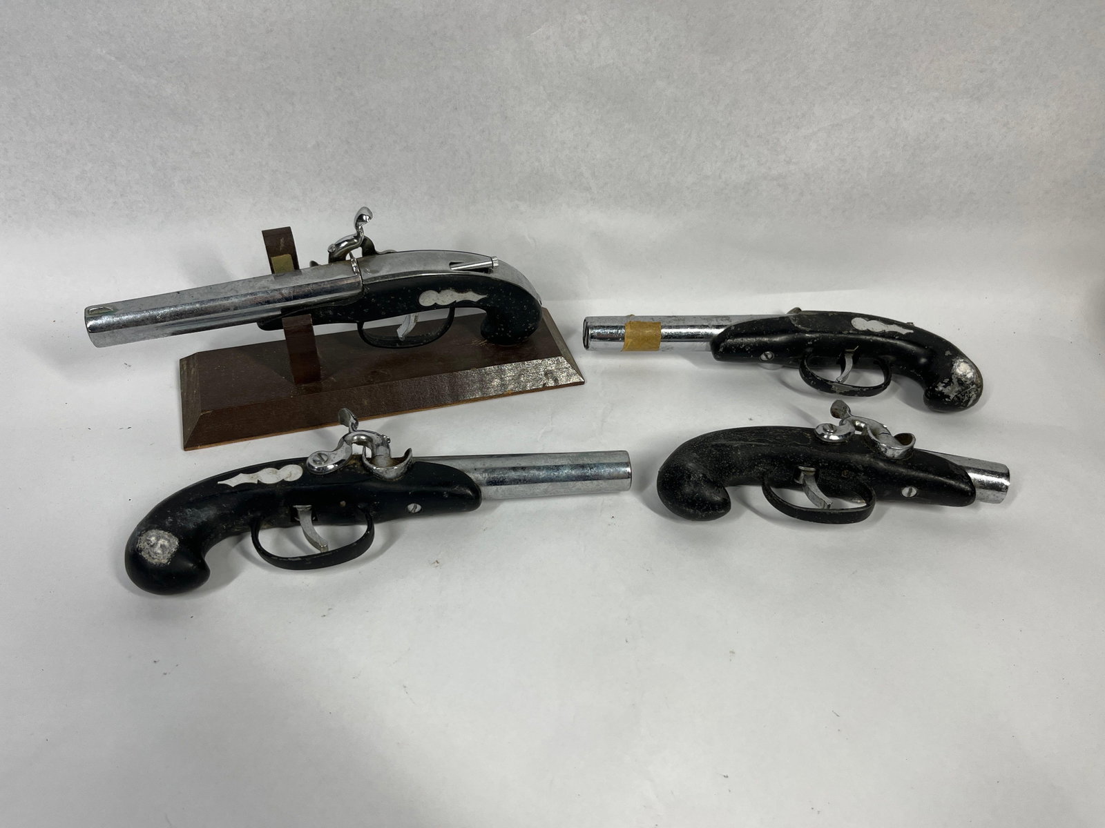 4 Japanese Flintlock Pistol Lighters: A Japanese collection of four vintage replica pistols styled after 18th and 19th-century flintlock firearms. These decorative items are designed as novelty table lighters, featuring chrome-plated