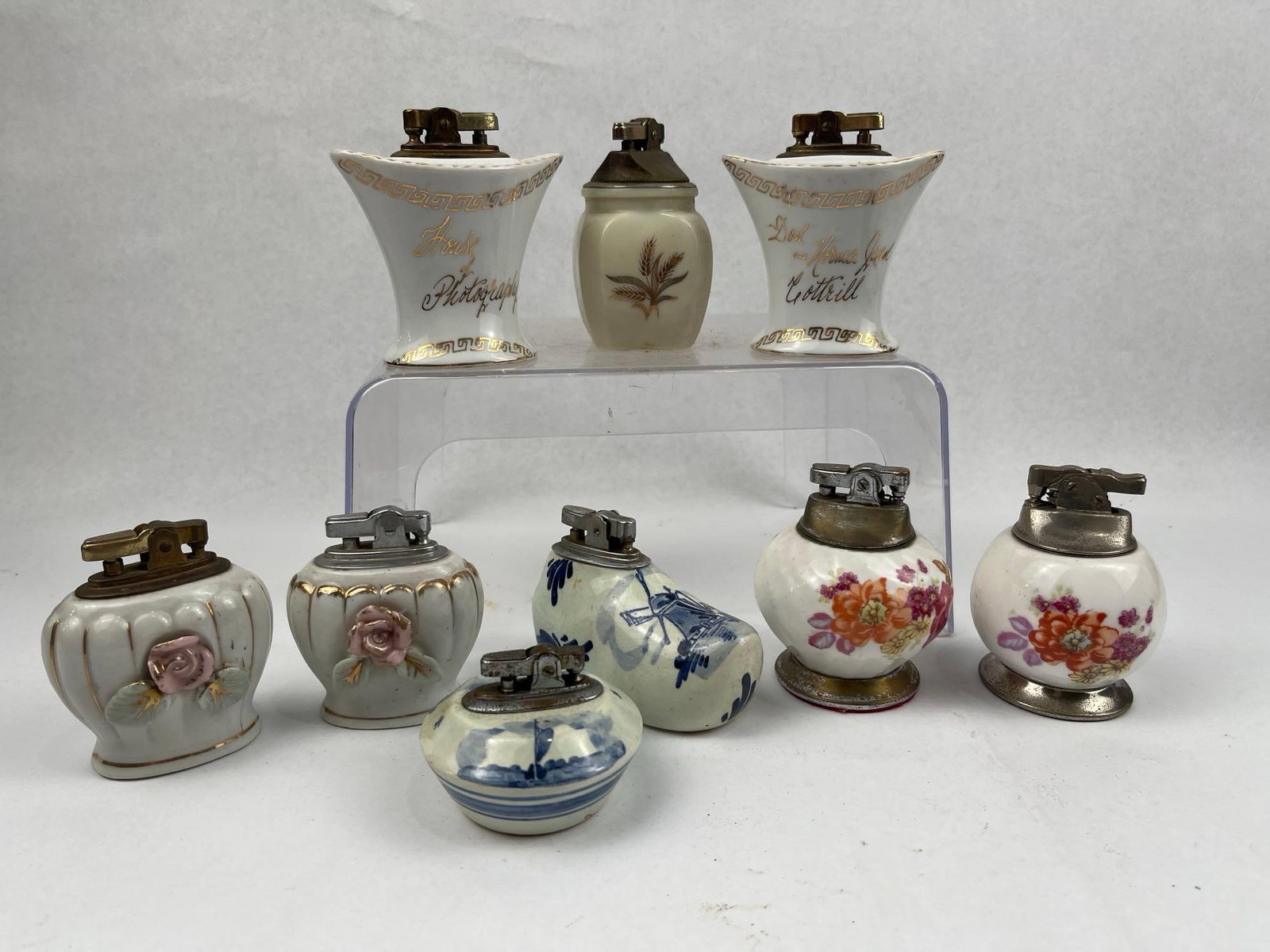 Vtg Porc. & Glass Table Lighters: This collection consists of several vintage table lighters in various decorative styles. The group includes a pair of white porcelain pedestal-style lighters with gold-toned Greek key borders; one is 