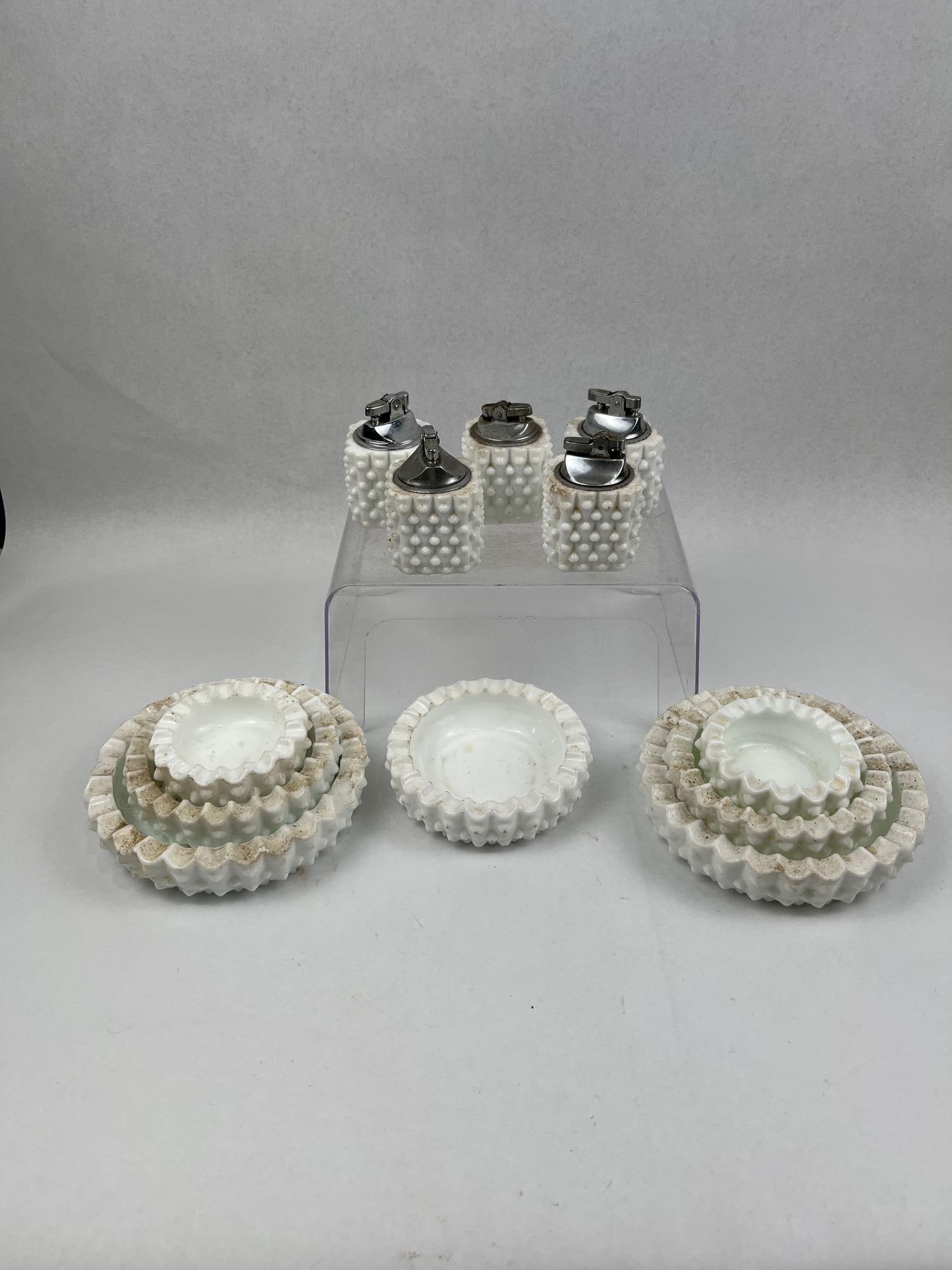 12pc Hobnail Milk Glass Lighter/Ashtray: A twelve-piece set of opaque white milk glass smoking accessories featuring an all-over hobnail pattern. The collection includes five cylindrical table lighters and seven nesting ashtrays. The ashtray