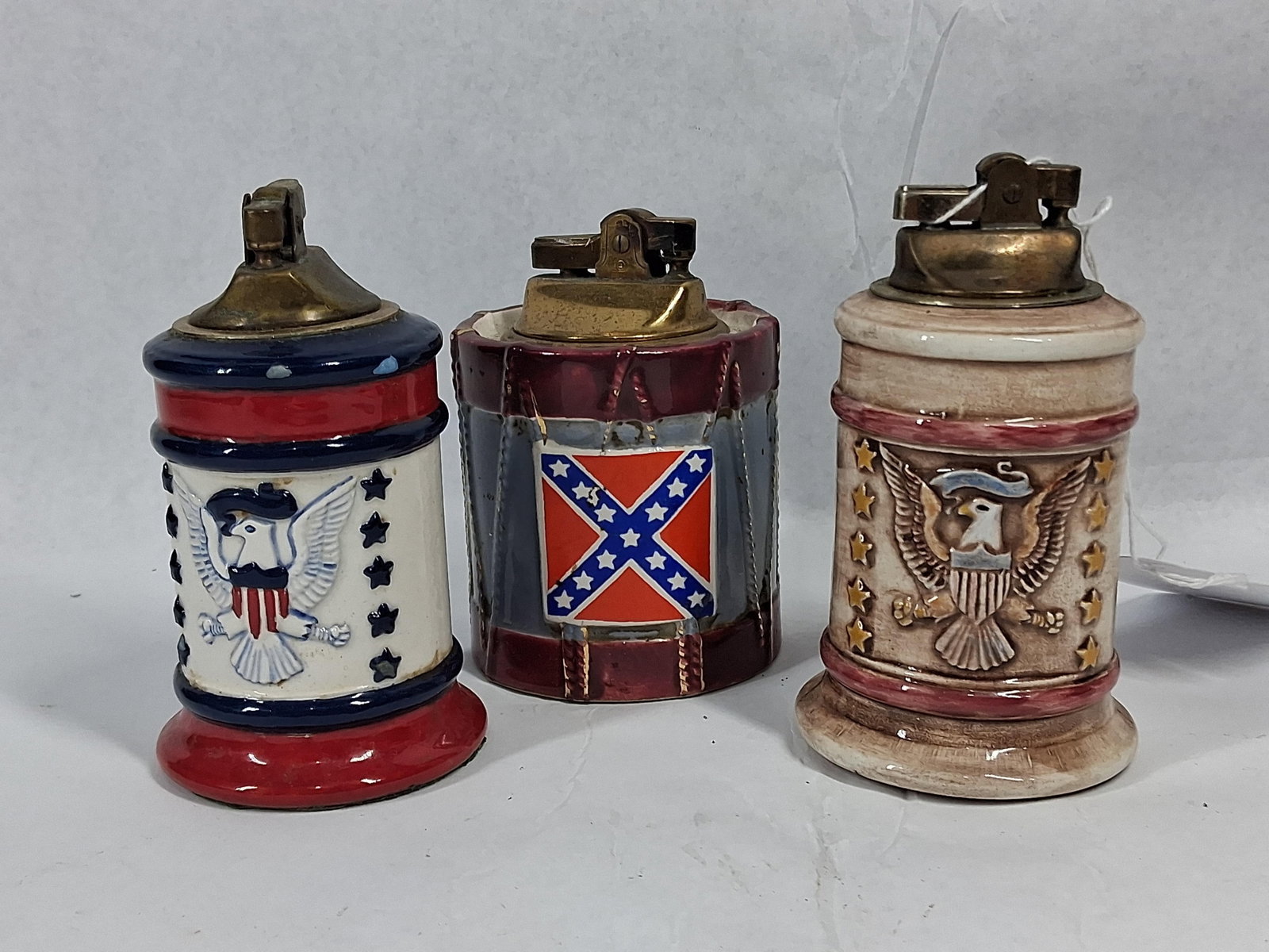 3 Japanese Ceramic Americana Lighters: A trio of Japanese ceramic table lighters featuring historical and patriotic motifs. The first lighter is cylindrical with a red, white, and blue design, decorated with a stylized eagle wearing a