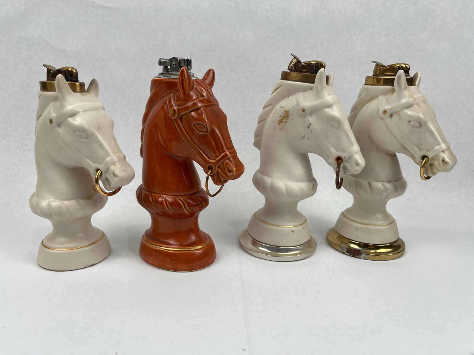 Evans Ceramic Horse Head Table Lighters: A collection of vintage Japanese-made glazed ceramic table lighters designed in the form of stylized horse heads, resembling traditional equestrian hitching posts or chess knights. The group includes 
