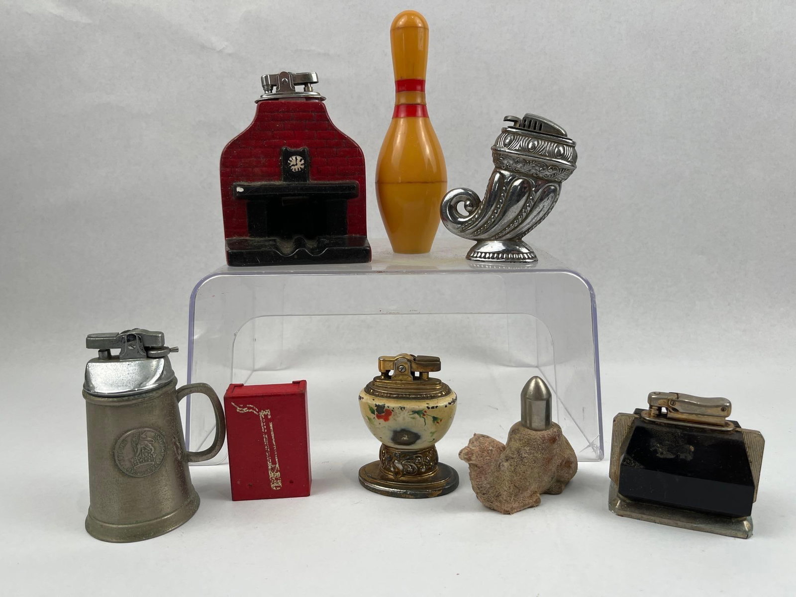Bentley & Occupied Japan Table Lighters: An assortment of mid-20th-century novelty table lighters and cigarette accessories in varied materials and forms. The collection includes a red brick-patterned fireplace lighter with an integrated ash
