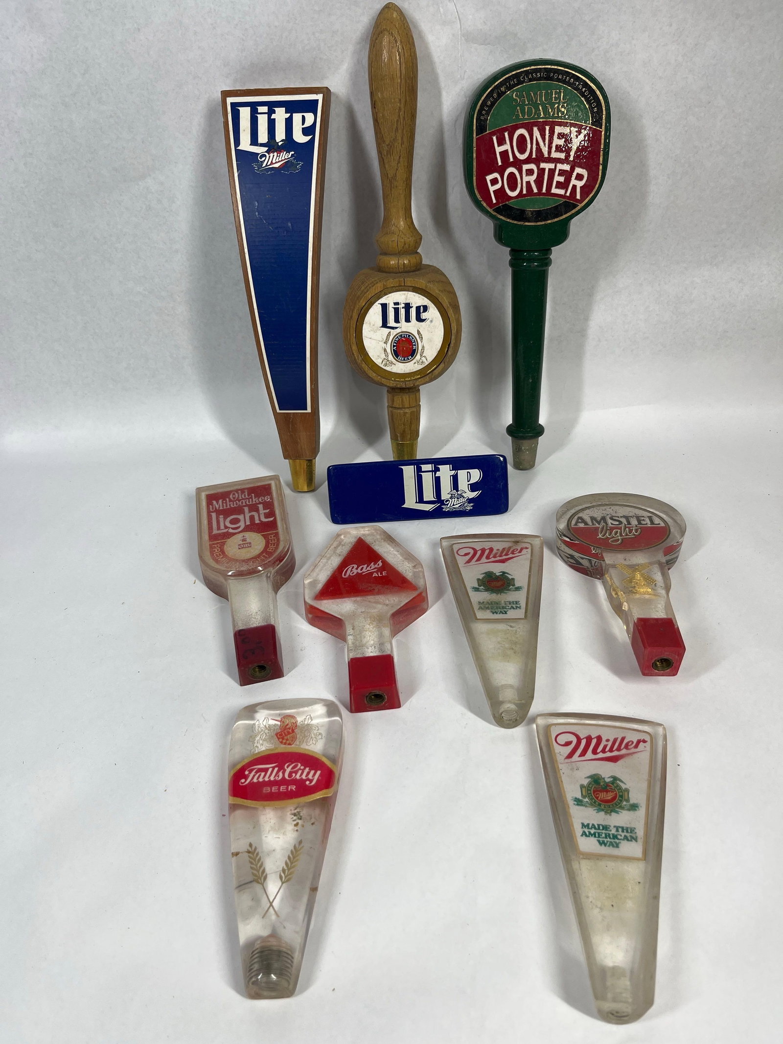 Vtg Miller, Sam Adams, Bass Tap Handles: A collection of vintage beer tap handles composed of various materials including turned wood, molded resin, and clear acrylic. The group features several brands with readable printed labels and