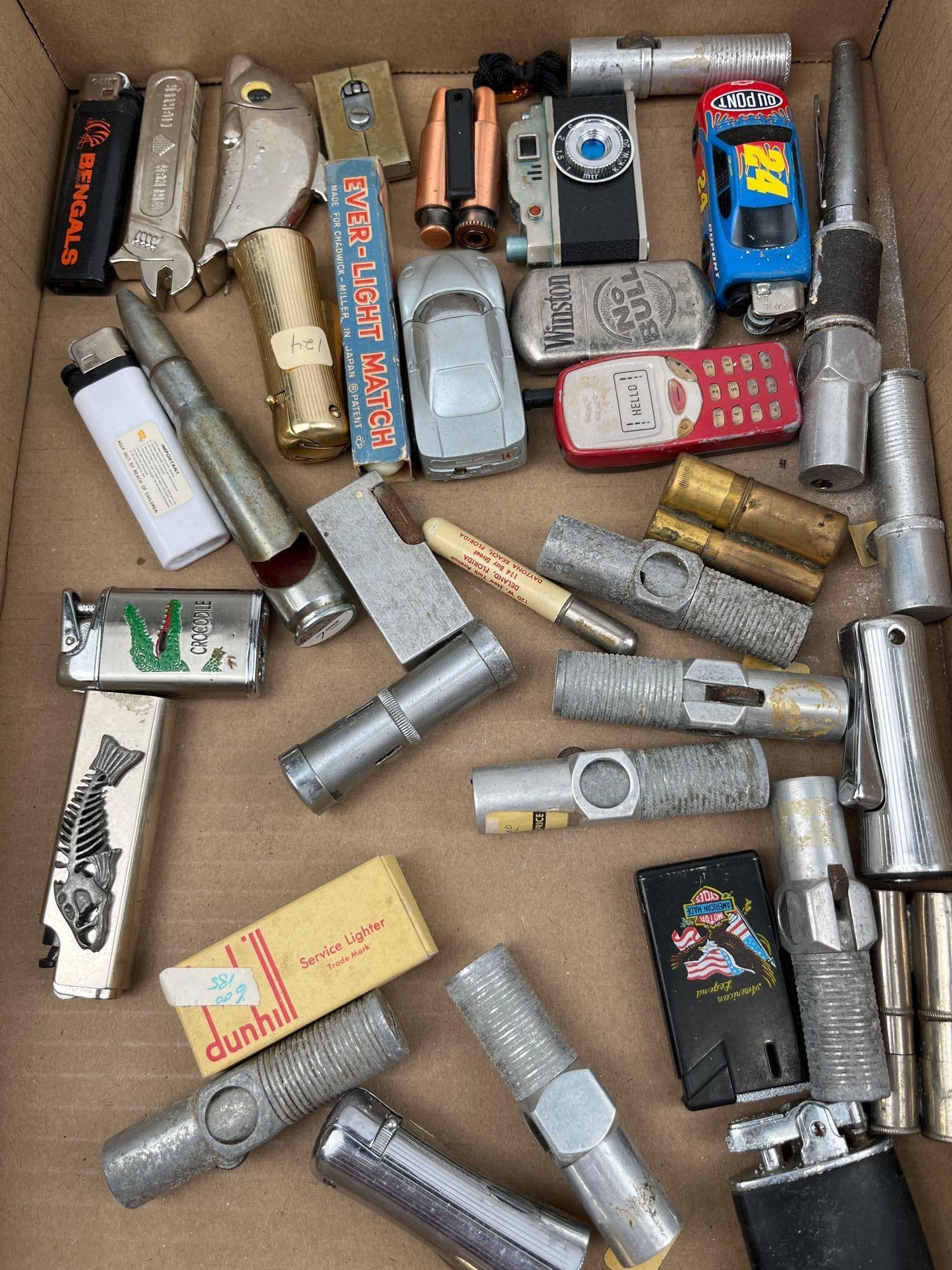Dunhill, Winston & NASCAR Vtg Lighters: An assortment of vintage lighters featuring a wide range of materials and novelty forms. The collection includes advertising pieces such as a black lighter with a printed BENGALS logo, a silver-tone f