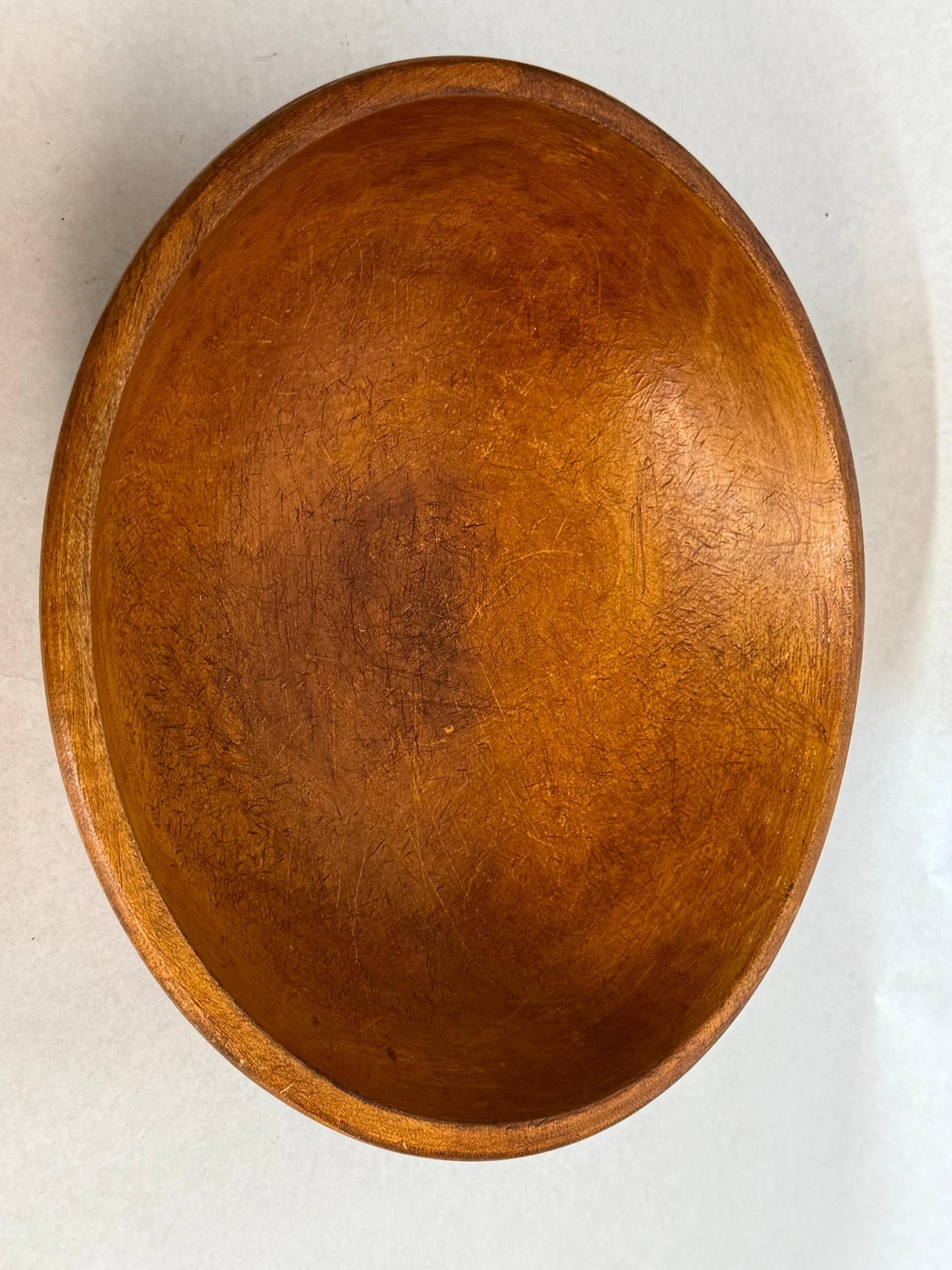 Munising Turned Wood Bowl: An American turned wood bowl of shallow rounded oval form featuring a flat base and a slightly defined rim. The piece is crafted from a light-grained wood with a honey-toned finish. The underside