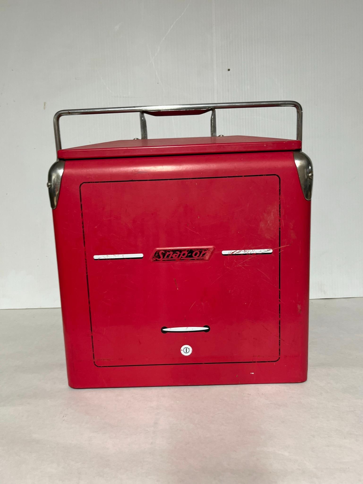 Snap-on Red Metal Picnic Cooler: A portable ice chest constructed with a red painted steel exterior and a metal-lined interior. The cooler features chrome-plated steel hardware, including corner guards and a large swing handle that