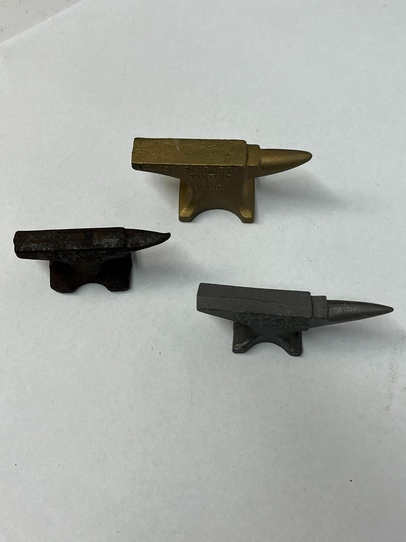 Trio Promotional Cast Metal Anvils: This lot features three miniature cast metal anvils produced as promotional items or salesman samples for industrial businesses. The first item is a brass-finished metal anvil. One side features