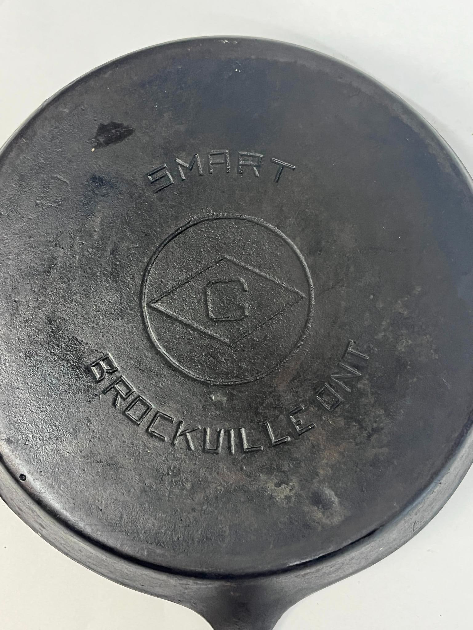 James Smart Mfg No. 9 Cast Iron Skillet: This is a cast iron skillet featuring two pouring spouts and a tapered handle with a teardrop-shaped hanging hole. In the center is an impressed circular mark containing a diamond shape with a