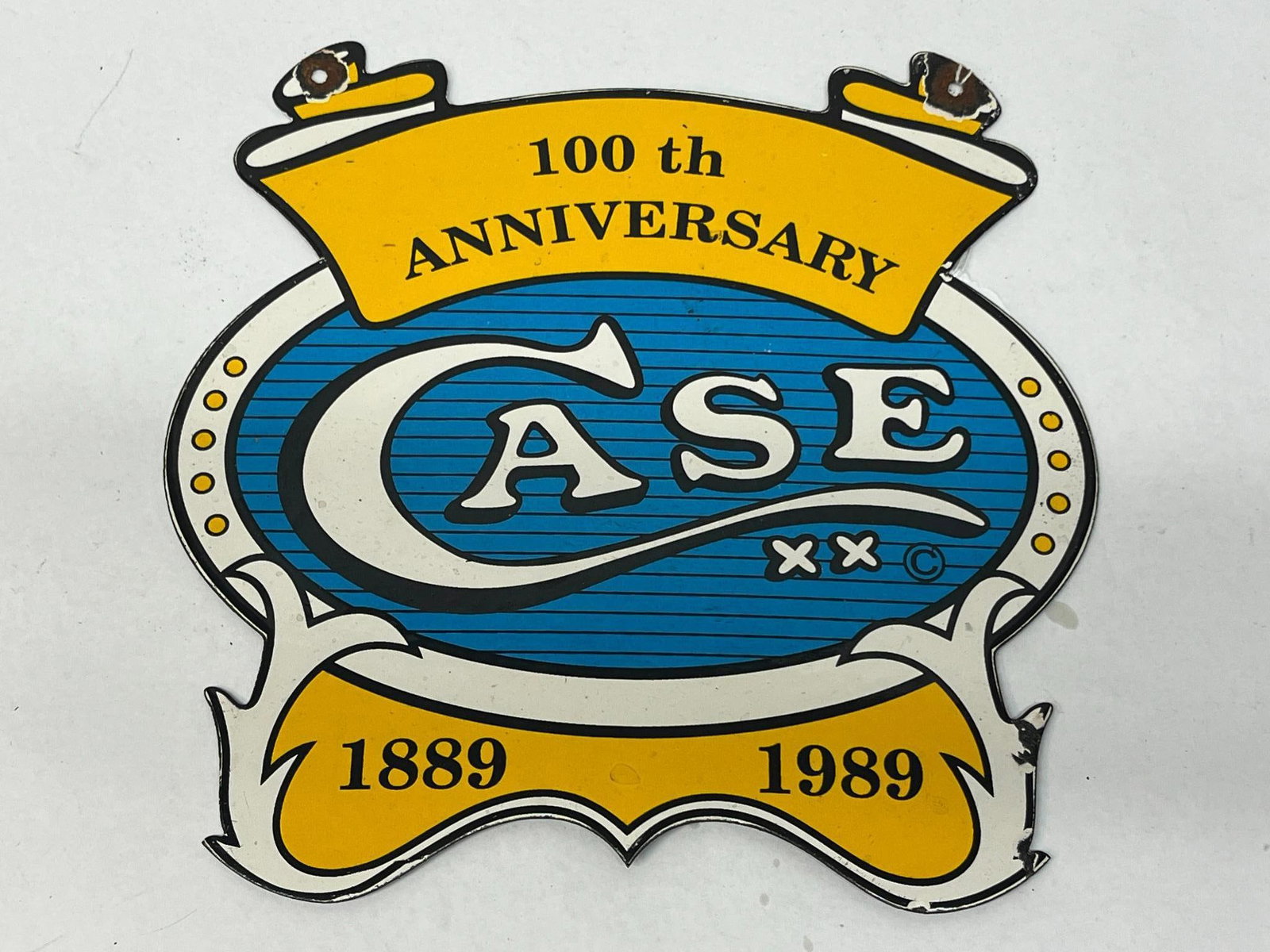 CASE 100th Anniversary Porc. Sign 1889: A die-cut porcelain enamel advertising sign commemorating the 100th anniversary of the W.R. The sign is constructed of heavy-gauge metal with a multi-colored porcelain finish. Above the oval is a