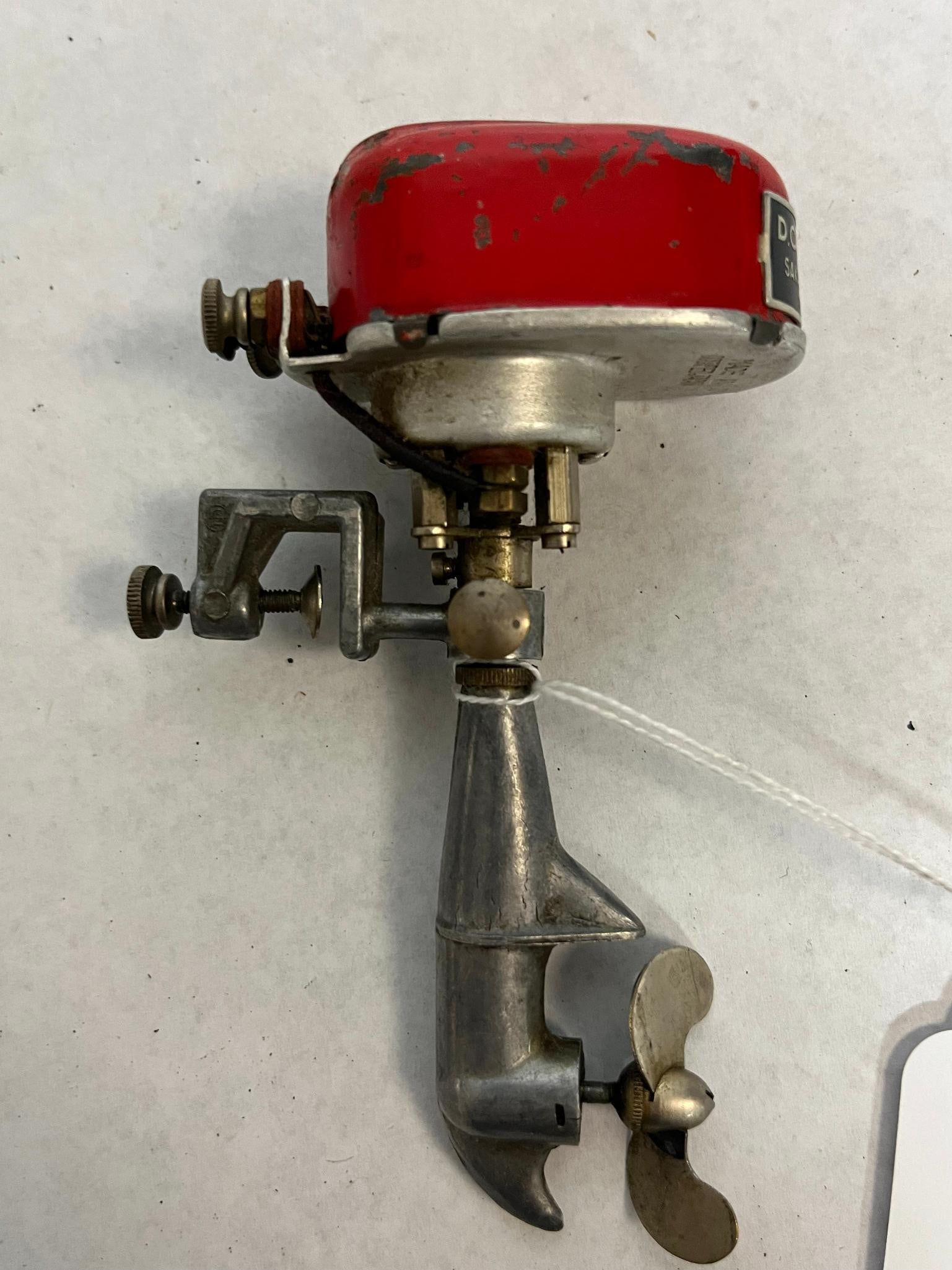 Sakai Seisakusho Toy Outboard Motor: A Japanese electric toy outboard motor for a boat. A black and silver rectangular adhesive label on the front of the red housing reads D.C. The underside of the cast metal base is embossed with the