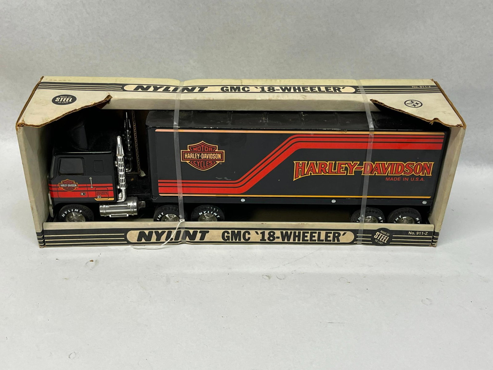 Nylint Harley-Davidson GMC Truck w/ Box: A Nylint GMC 18-Wheeler semi-tractor and trailer toy set featuring Harley-Davidson branding. The toy is constructed of pressed steel with a black baked enamel finish, accented by orange and red graphi