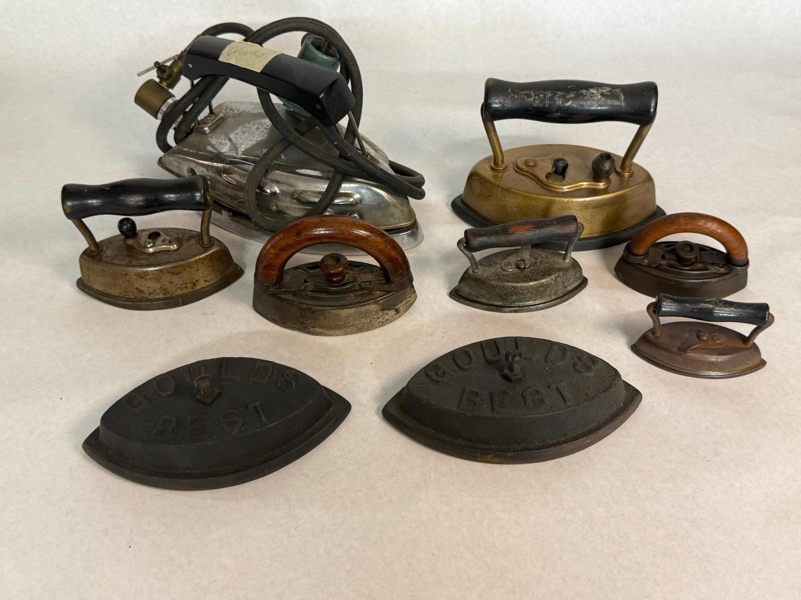 Goulds Best Bases & Antique Irons: An assortment of antique and irons featuring various heating technologies, materials, and designs. The collection includes two detachable cast iron bases. These bases feature an impressed mark with